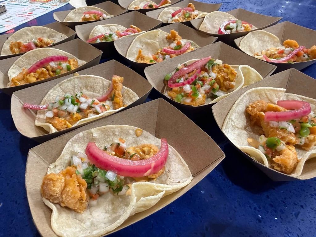 A variety of tacos with crispy fried toppings, fresh salsa, and pickled onions, served in disposable paper boats in Atlanta, Georgia.