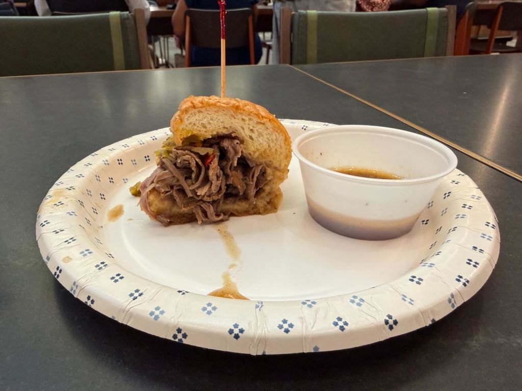 A pulled pork sandwich with a side of dipping sauce on a paper plate in Atlanta, Georgia.