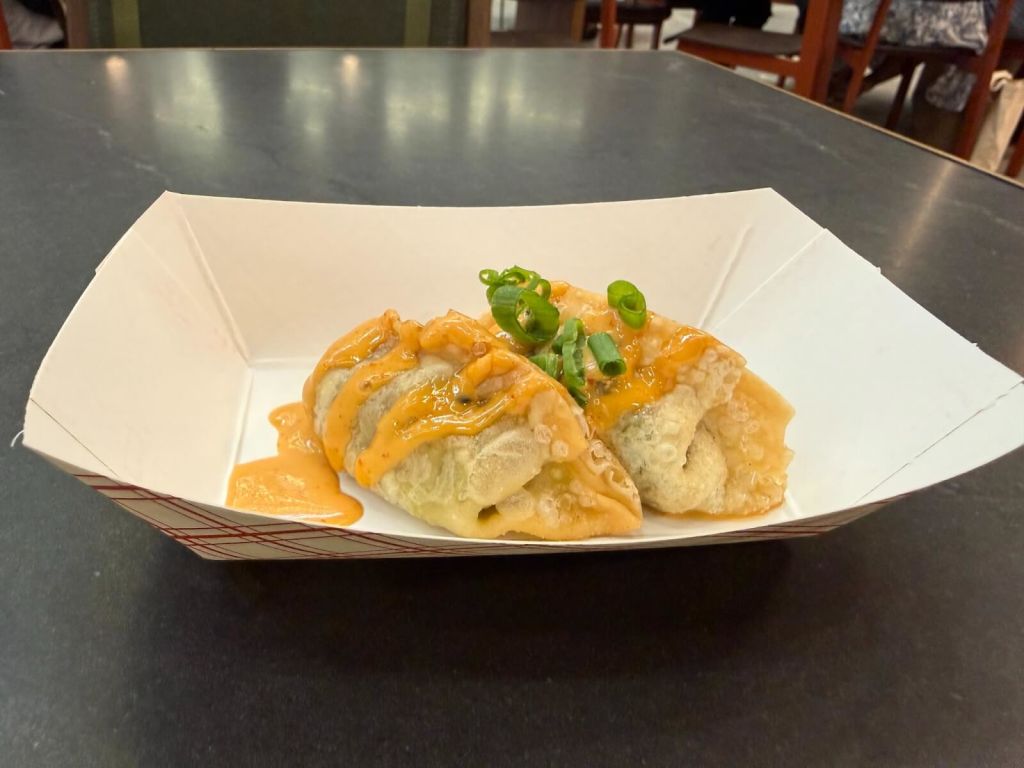 Two crispy, golden-brown dumplings topped with a creamy orange sauce and garnished with chopped green onions in Atlanta, Georgia.