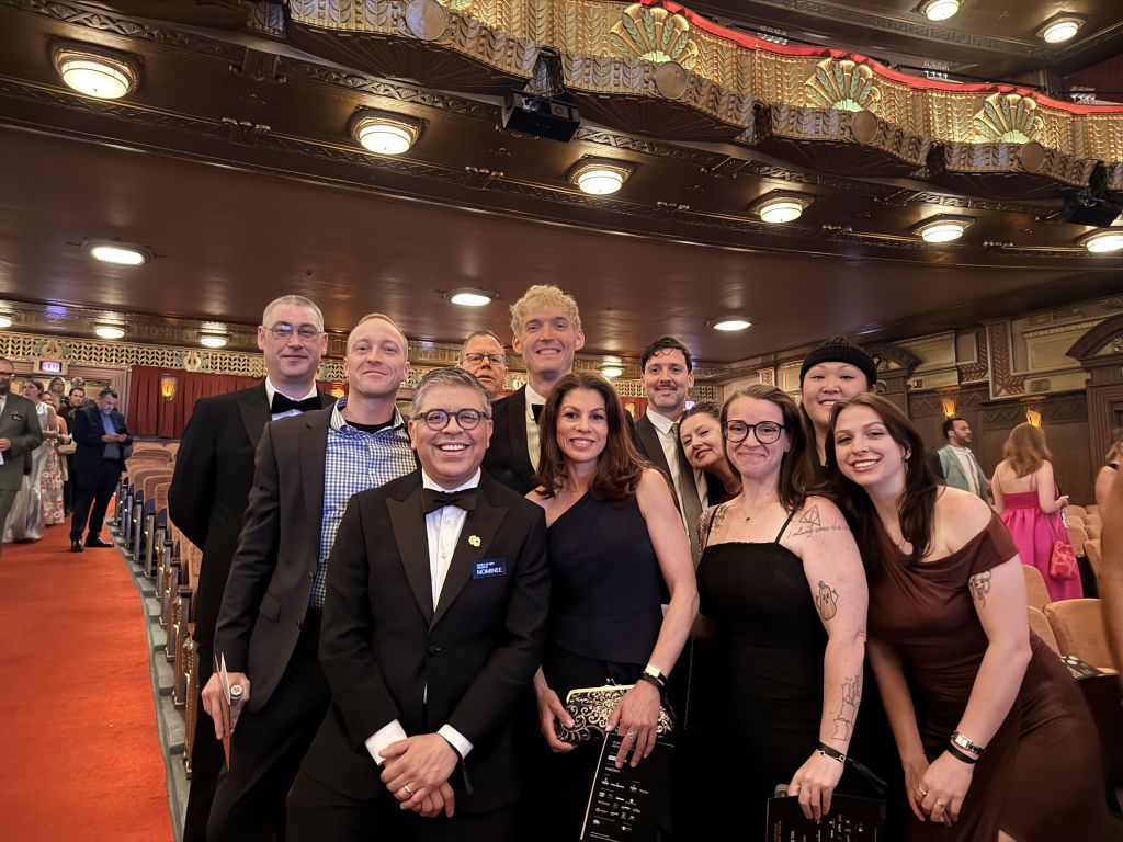 A group of elegantly dressed people pose for a photo in a lavish theater lobby with ornate ceilings and red carpet in Atlanta, Georgia.