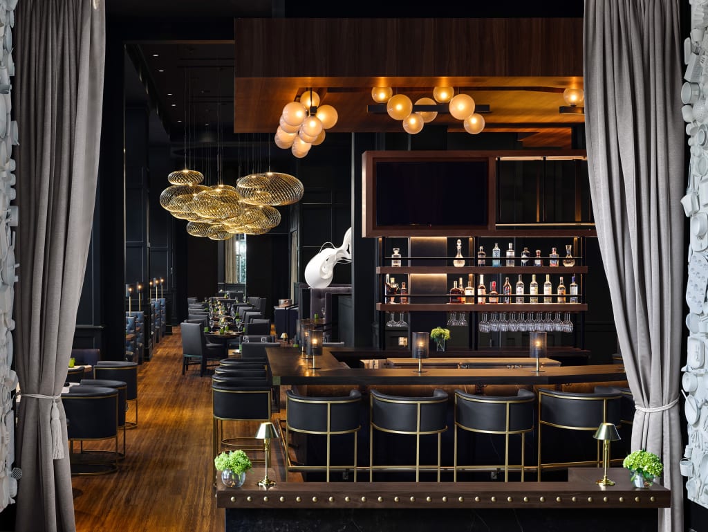 A modern, upscale bar with a curved wooden counter, black leather stools, and a sophisticated lighting design in Atlanta, Georgia.