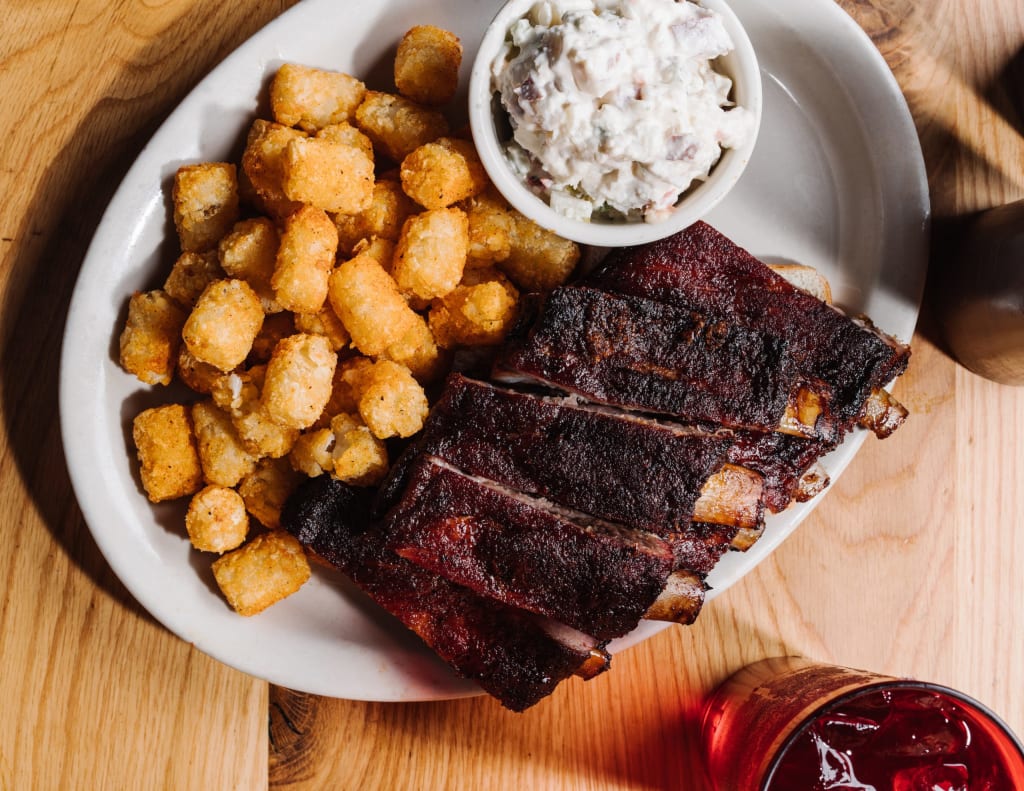 A plate of barbecue ribs with tater tots and coleslaw on a wooden table in Atlanta, Georgia.