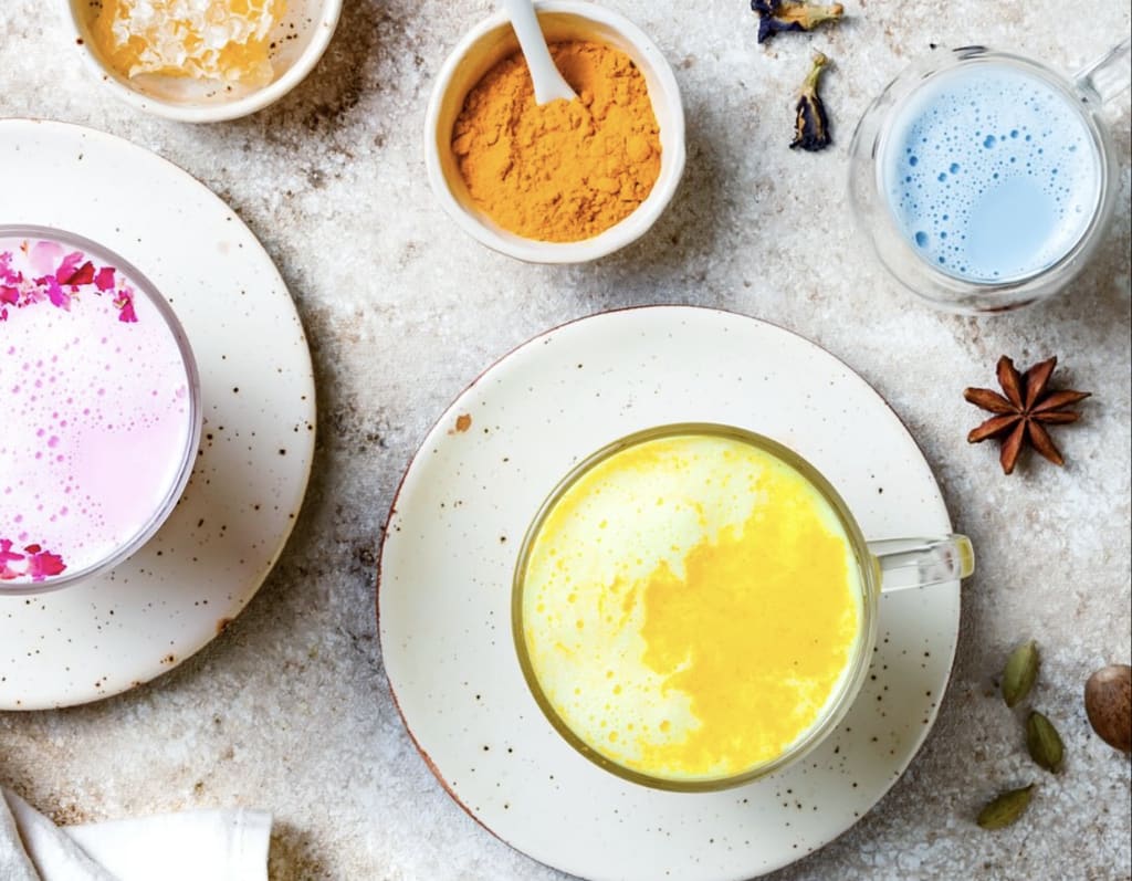 Three colorful lattes with turmeric, matcha, and rose petal toppings on speckled plates in Atlanta, Georgia.