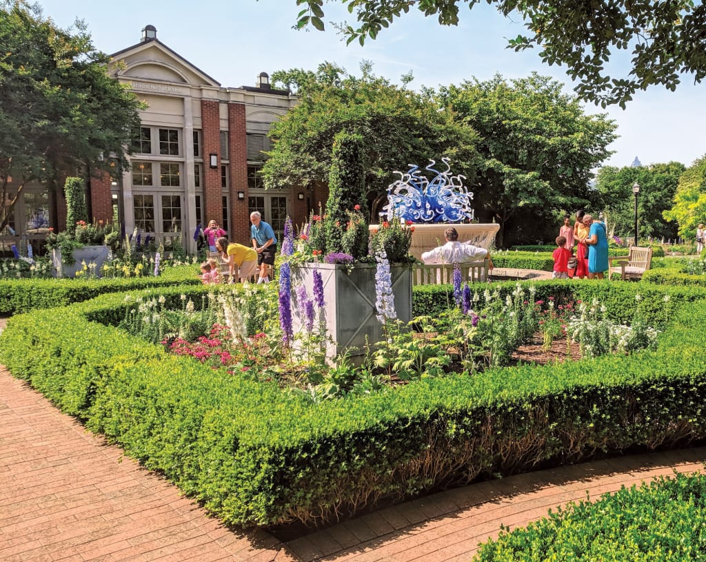 A vibrant garden with colorful flowers, manicured hedges, and a blue glass sculpture in Atlanta, Georgia.