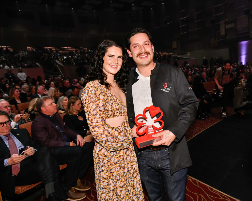 La Guía MICHELIN Regresa a Atlanta 7 A couple smiles while holding a red award in front of an audience in Atlanta, Georgia.