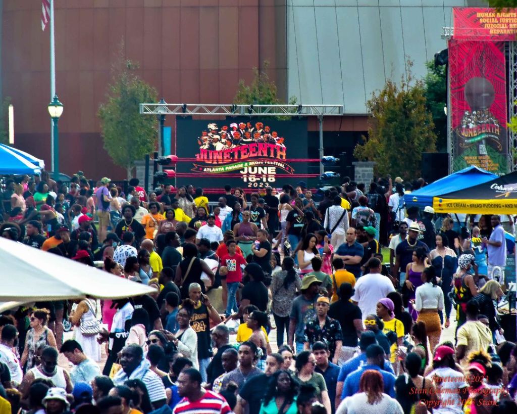 A large, diverse crowd gathers at an outdoor festival with tents and stages in Atlanta, Georgia.