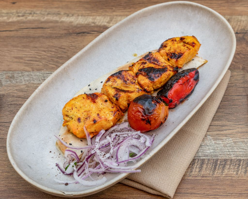 Grilled chicken skewers with charred vegetables and sliced onions on a white plate in Atlanta, Georgia.
