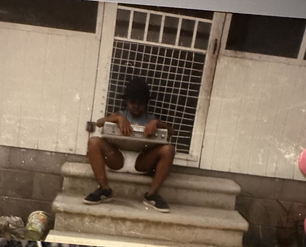 A young child sits on concrete steps, holding a metal object, with a window and door behind them in Atlanta, Georgia.