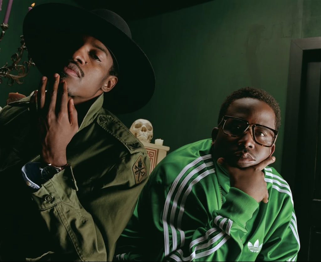 Two men in green military-style jackets pose together, one wearing a wide-brimmed hat in Atlanta, Georgia.