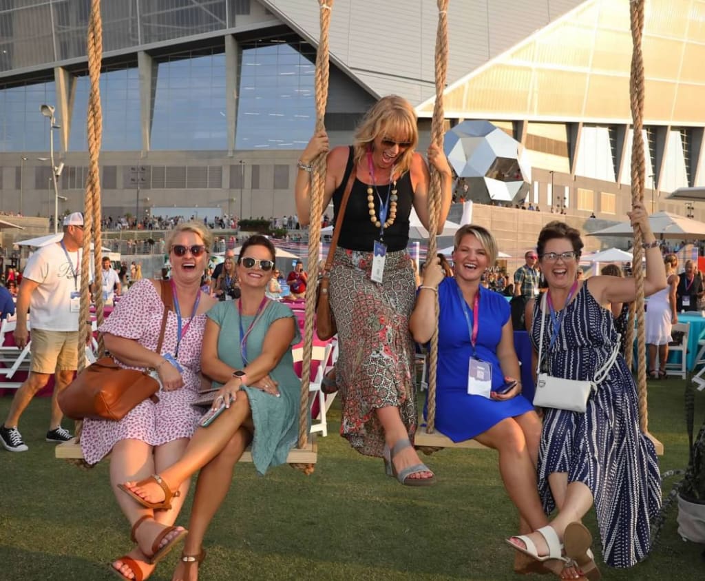 Five women swing together on a rope swing at an outdoor event, laughing and enjoying the moment in Atlanta, Georgia.