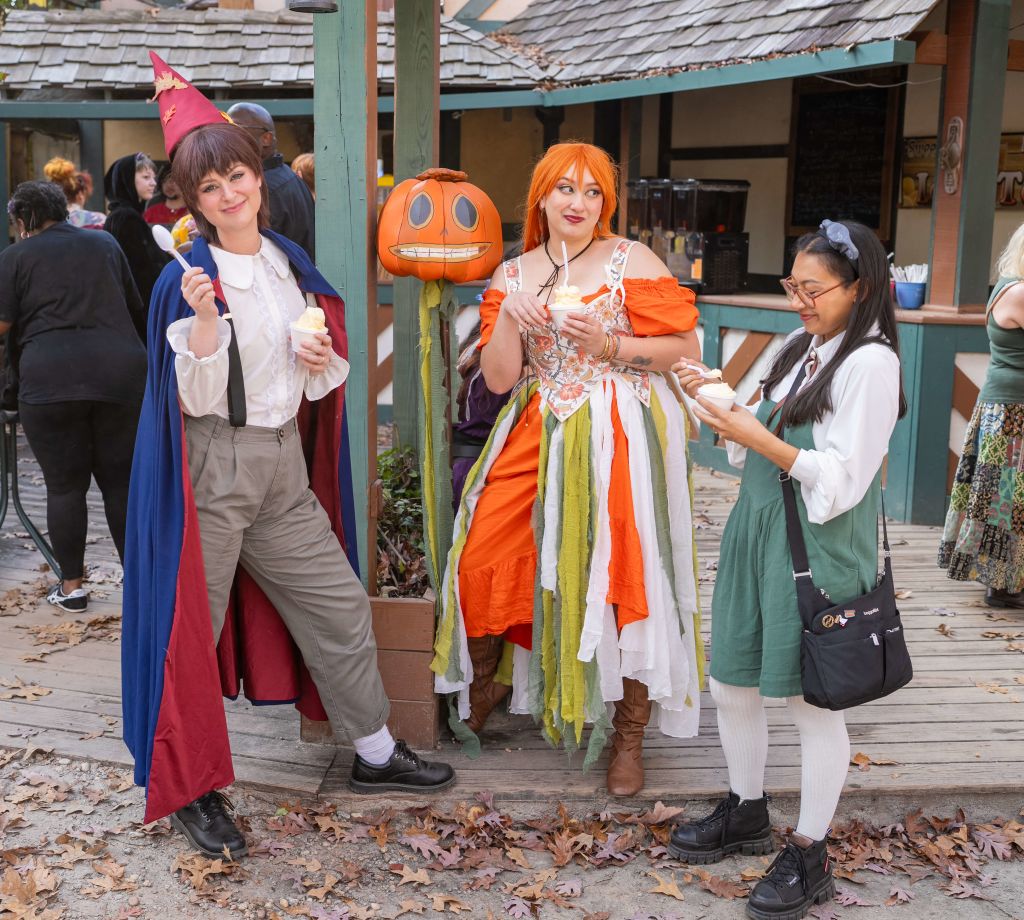 Three women dressed in whimsical Halloween costumes enjoy ice cream cones together at an outdoor event in Atlanta, Georgia.