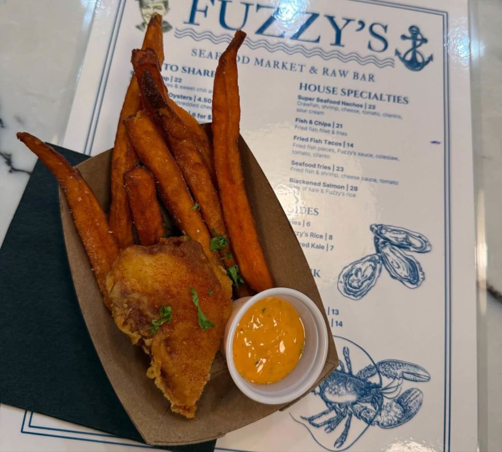 A basket of crispy sweet potato fries and a piece of fried chicken served with a side of orange sauce at Fuzzy's Market & Raw Bar in Atlanta, Georgia.