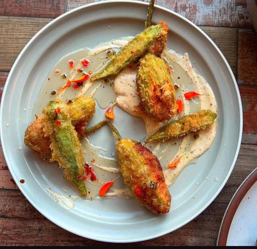 A plate of crispy fried zucchini blossoms with a creamy sauce and edible flowers in Atlanta, Georgia.