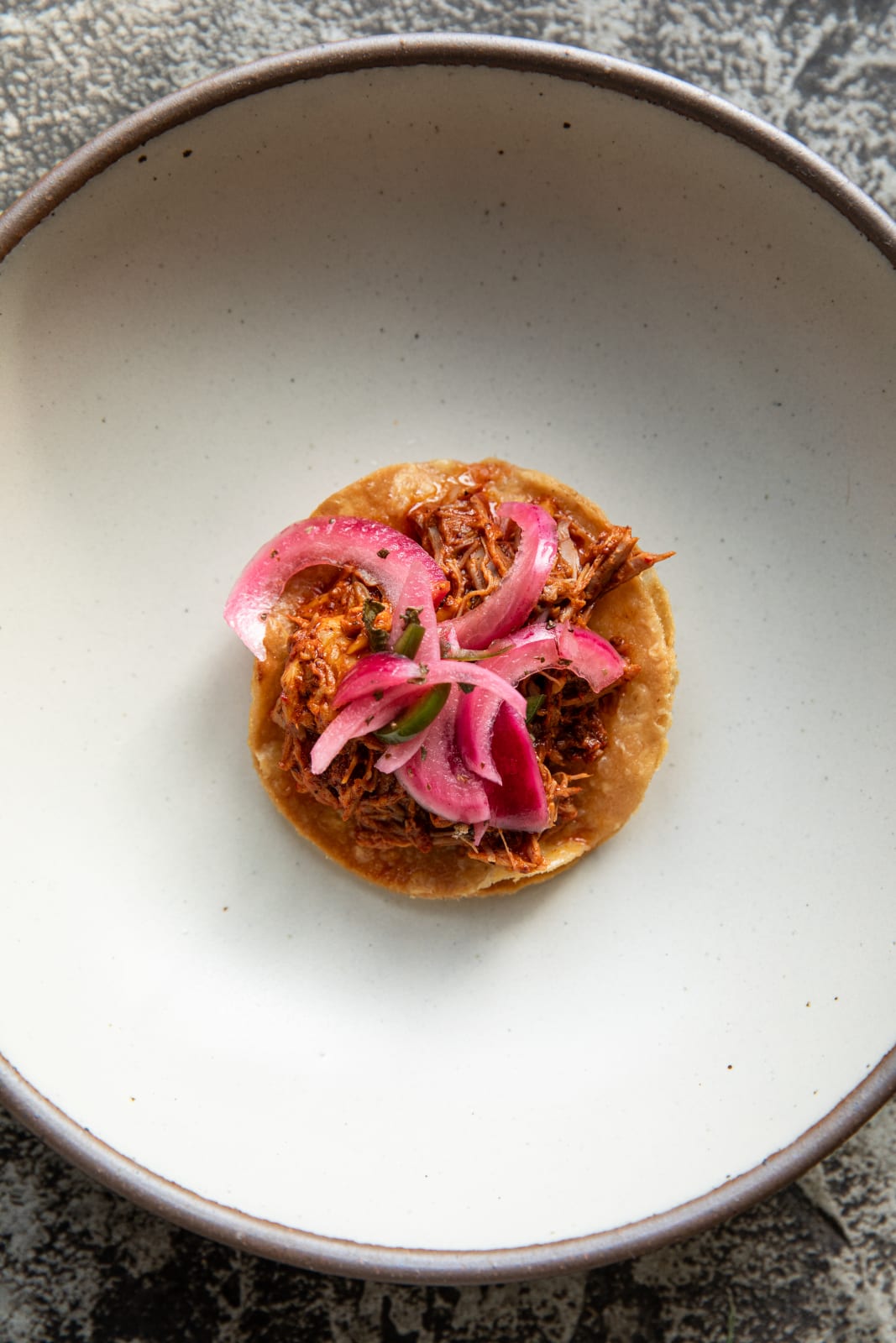 A single taco with shredded meat, pickled onions, and cilantro on a white plate in Atlanta, Georgia.