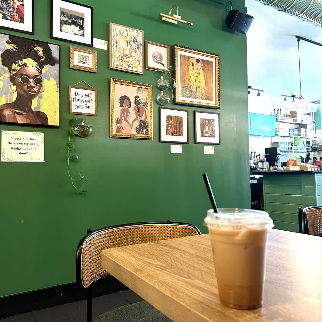 A vibrant green wall adorned with eclectic framed art and a hanging plant in a cozy café setting in Atlanta, Georgia.