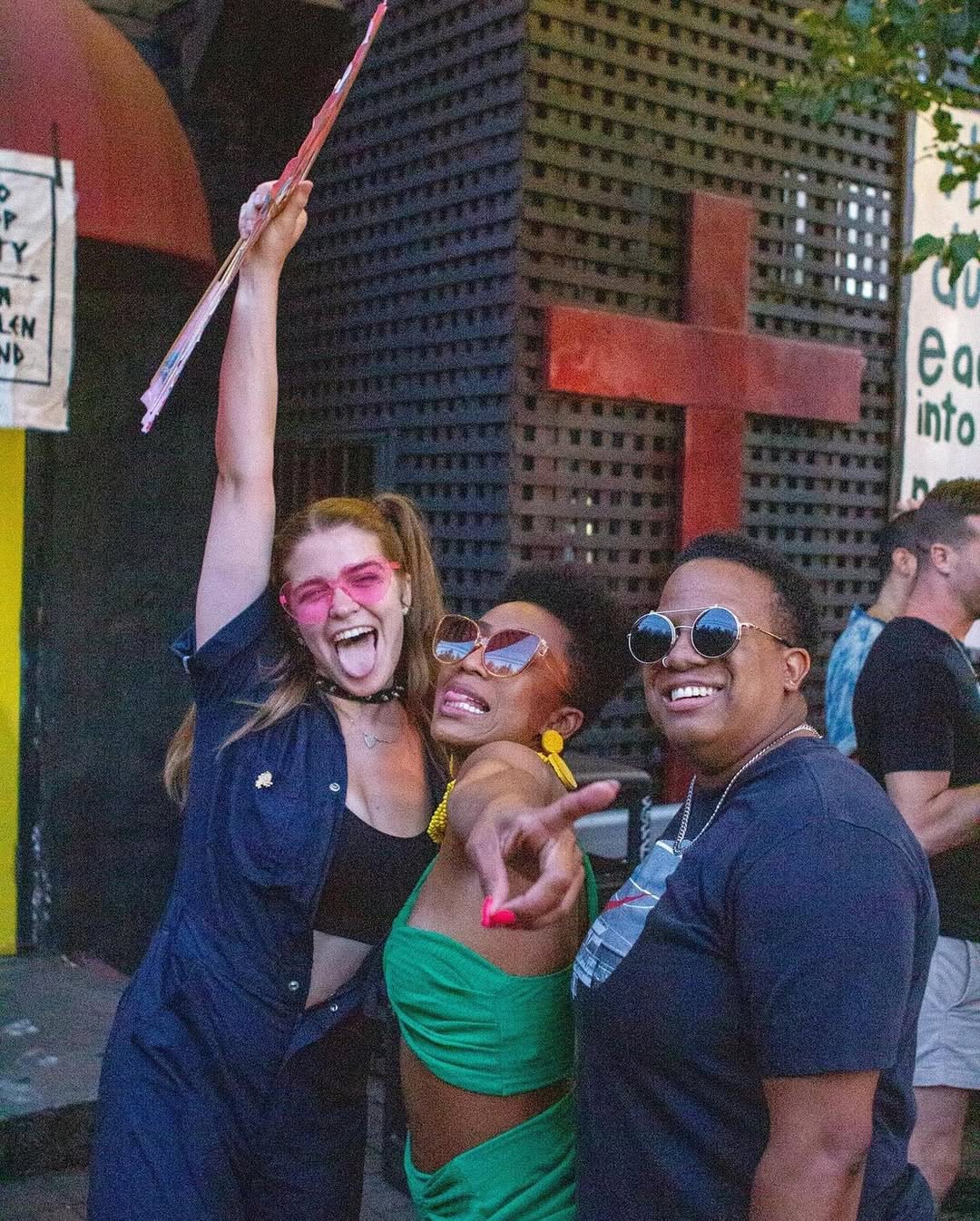 Three women pose joyfully together, one holding a sign, in front of a colorful building in Atlanta, Georgia.