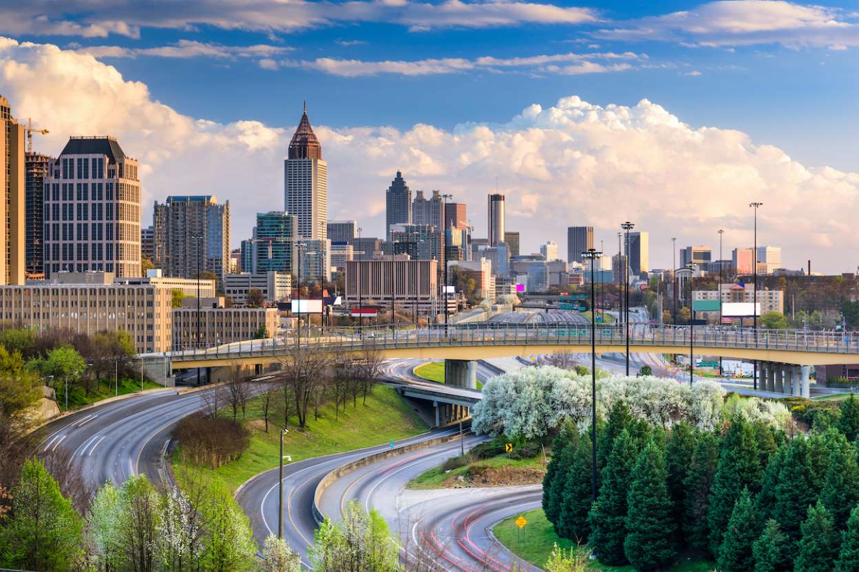 DISCOVER ATL HOP & RIDE 1 Aerial view of a sprawling cityscape with tall skyscrapers and winding highways surrounded by lush greenery in Atlanta, Georgia.