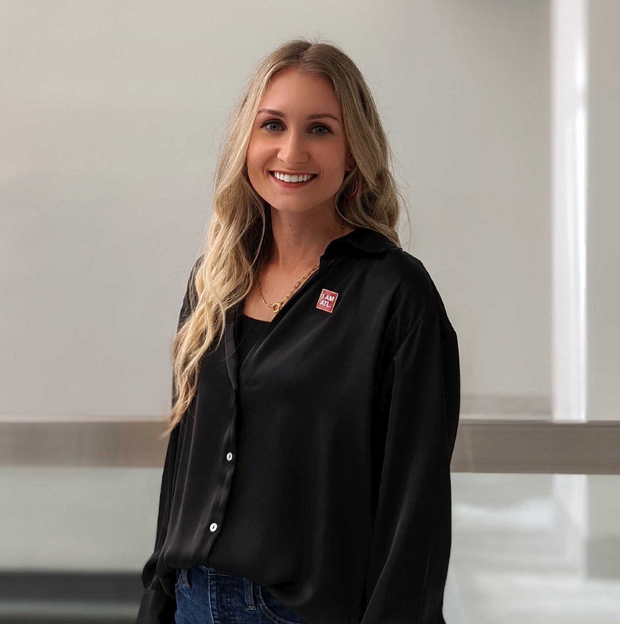 A smiling woman with long blonde hair wearing a black shirt stands indoors in Atlanta, Georgia.