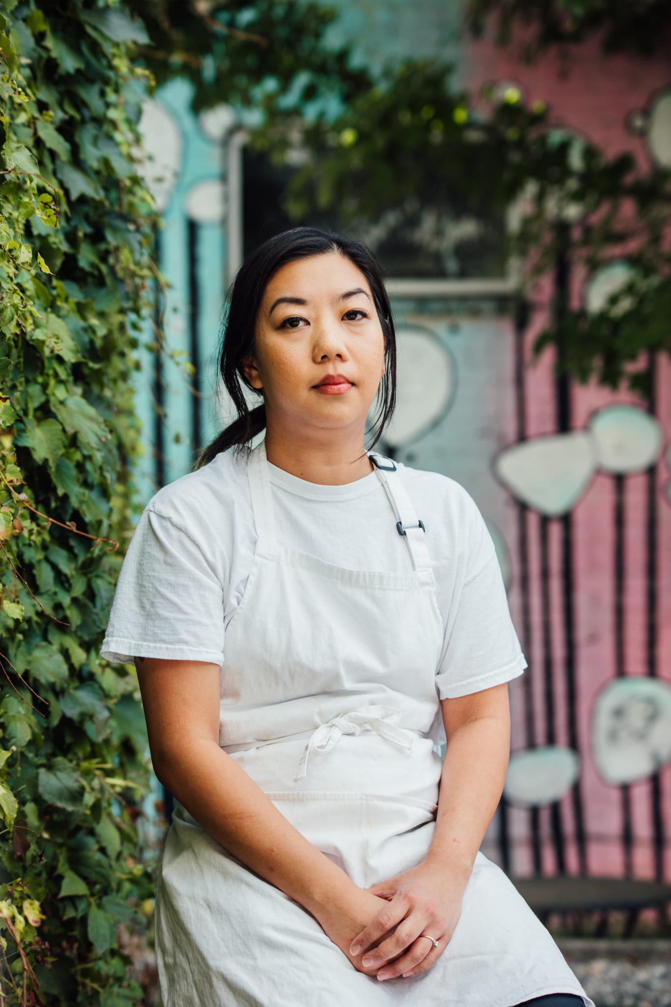 A woman in a white apron sits against a colorful mural with green foliage in Atlanta, Georgia.