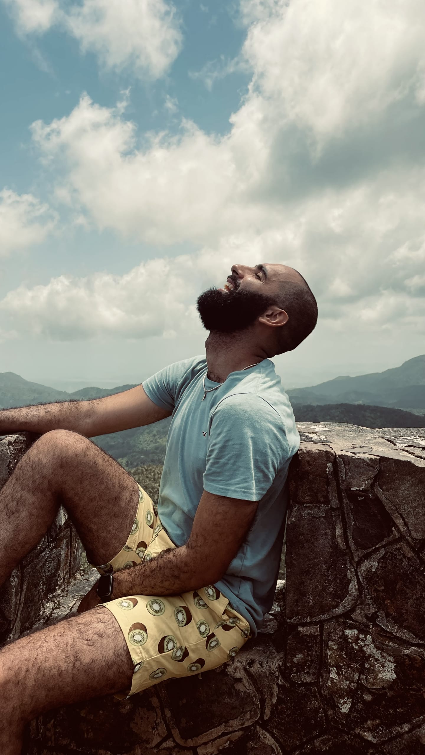 Angel Fabián Rivera 2 A bald man with a beard sits on a stone wall, gazing up at the cloudy sky in a serene pose in Atlanta, Georgia.