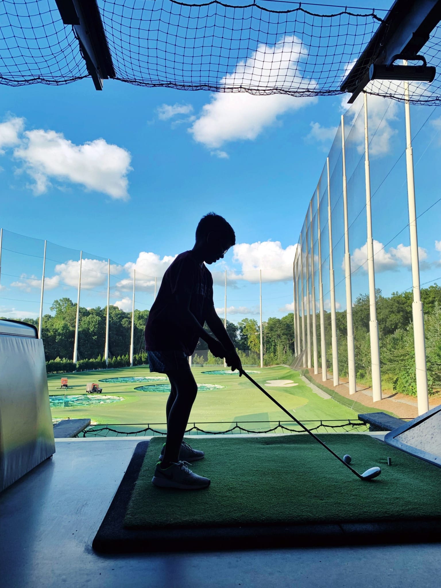 A young golfer practices his swing on a driving range with a clear blue sky above in Atlanta, Georgia.