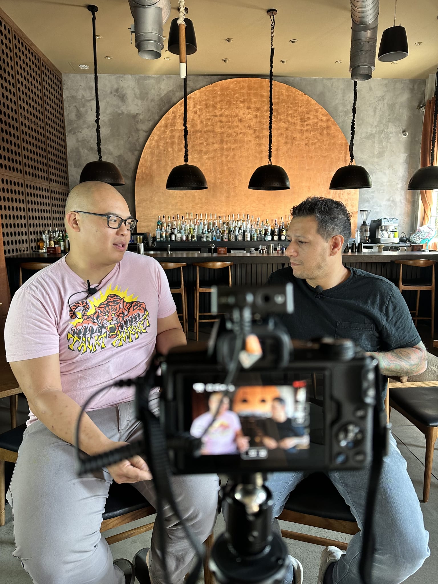 Two men sit in a bar, one with a camera, filming an interview with the other in Atlanta, Georgia.