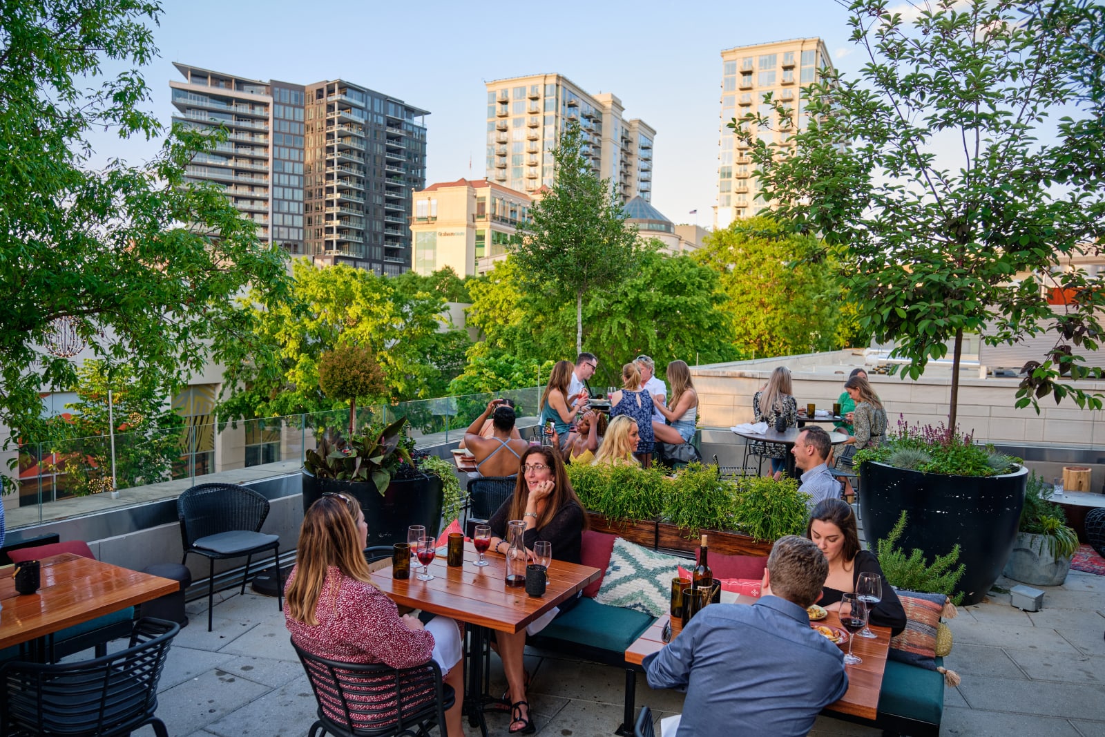 People enjoying drinks and conversation at an outdoor rooftop bar surrounded by greenery and city skyline in Atlanta, Georgia.