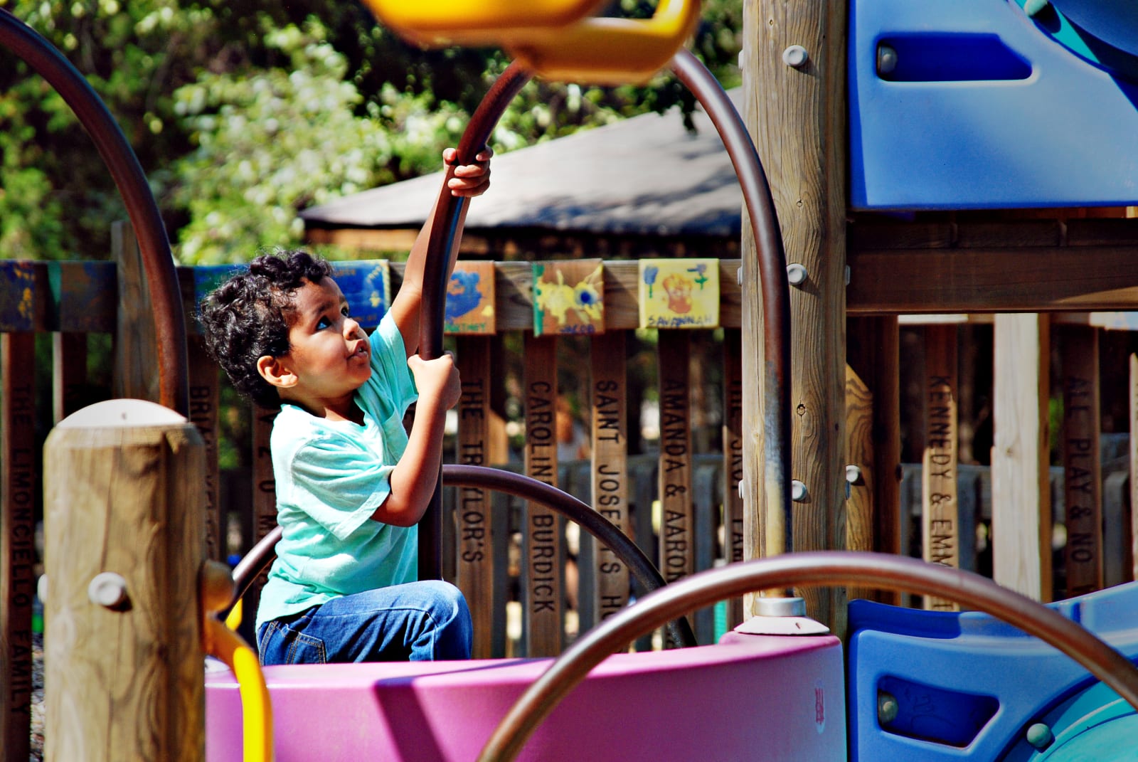 Best Atlanta Playgrounds for Kids of All Ages 9 A young child plays on a colorful playground structure, reaching up to hold a metal bar in Atlanta, Georgia.