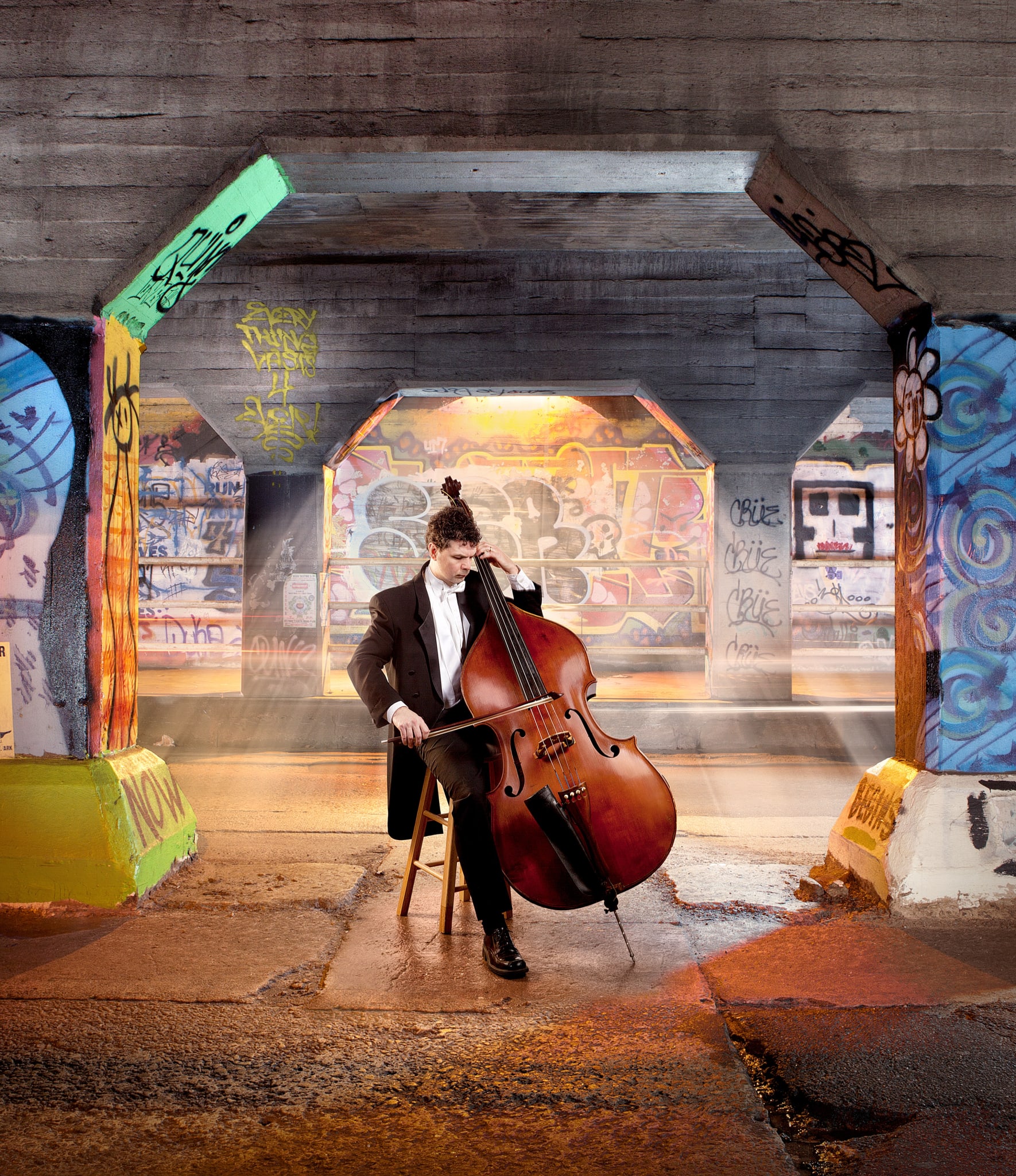 A musician in formal attire plays a cello in a graffiti-covered underpass in Atlanta, Georgia.