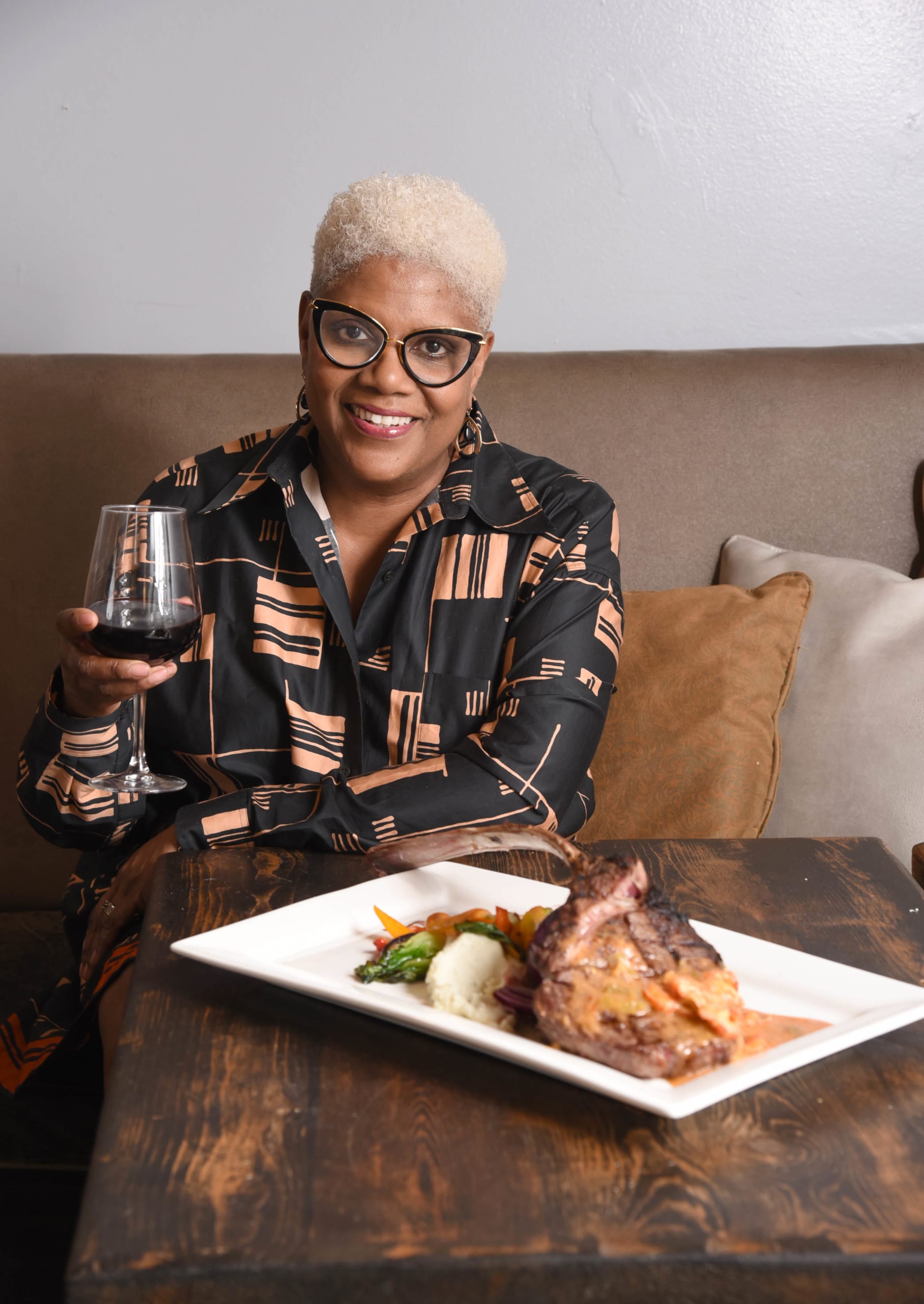 A woman with short blonde hair and glasses is smiling while holding a glass of red wine in Atlanta, Georgia.