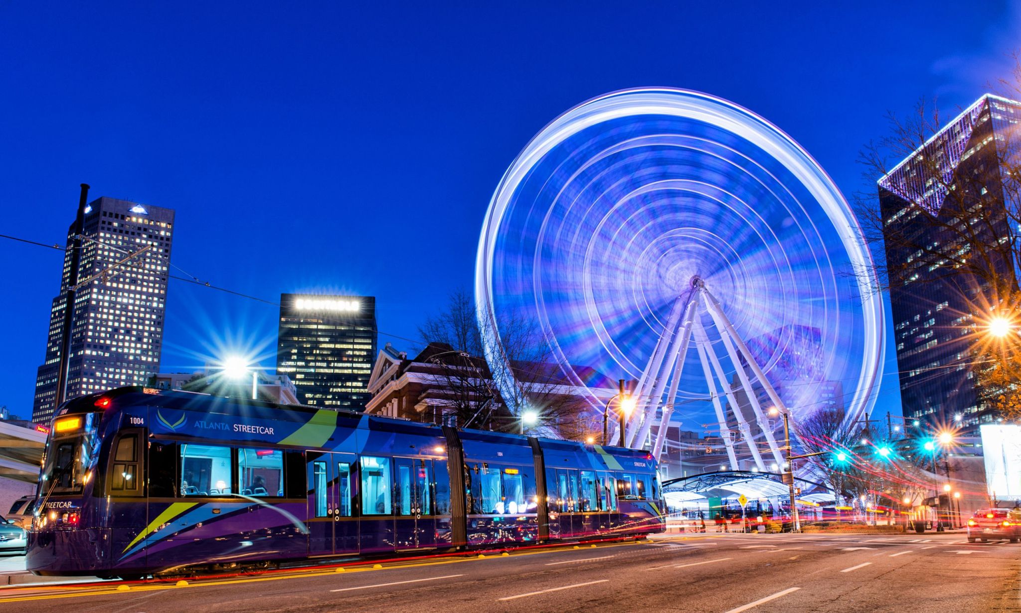 Guide to Exploring Atlanta on MARTA Trains (From a Local) 1 A vibrant cityscape at night featuring a blue-lit Ferris wheel, modern tram, and illuminated skyscrapers in Atlanta, Georgia.