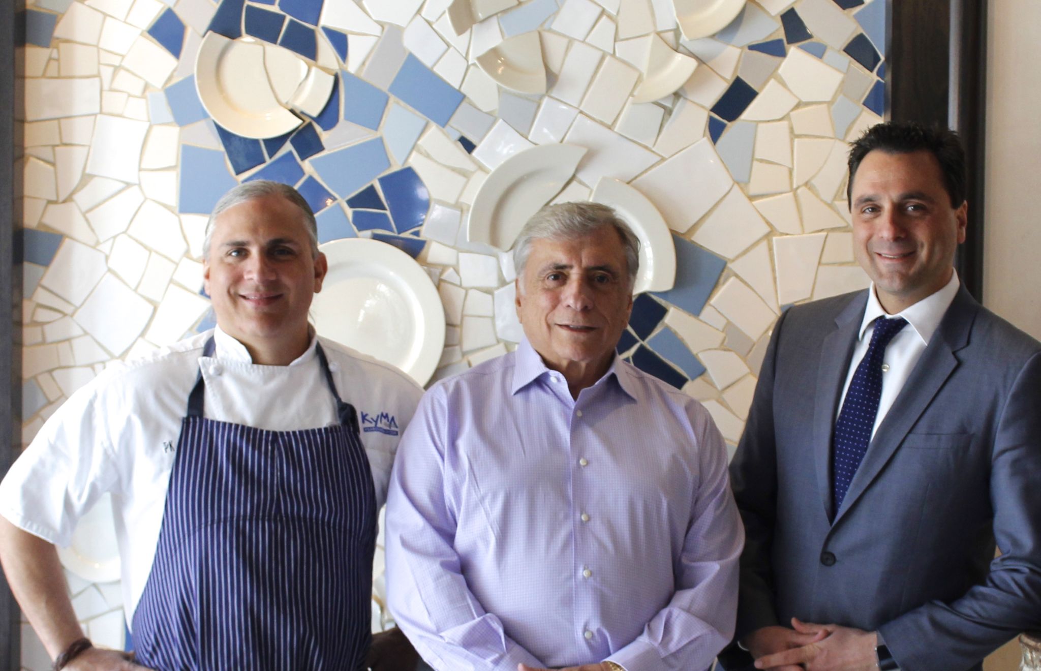 Three men posing. One in chef jacket and two in business attire.