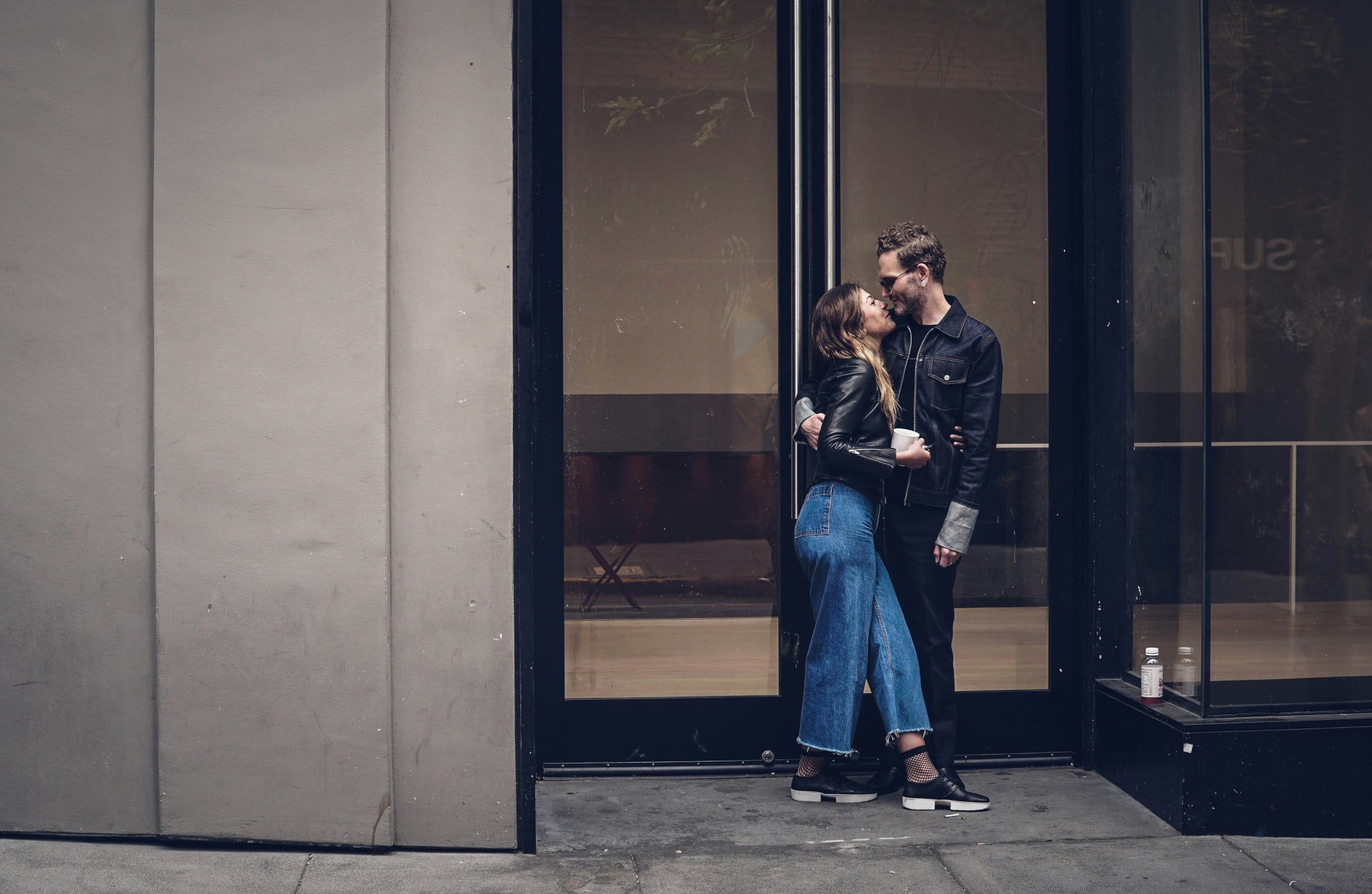 A couple embraces outside a modern building with glass doors and concrete walls in Atlanta, Georgia.
