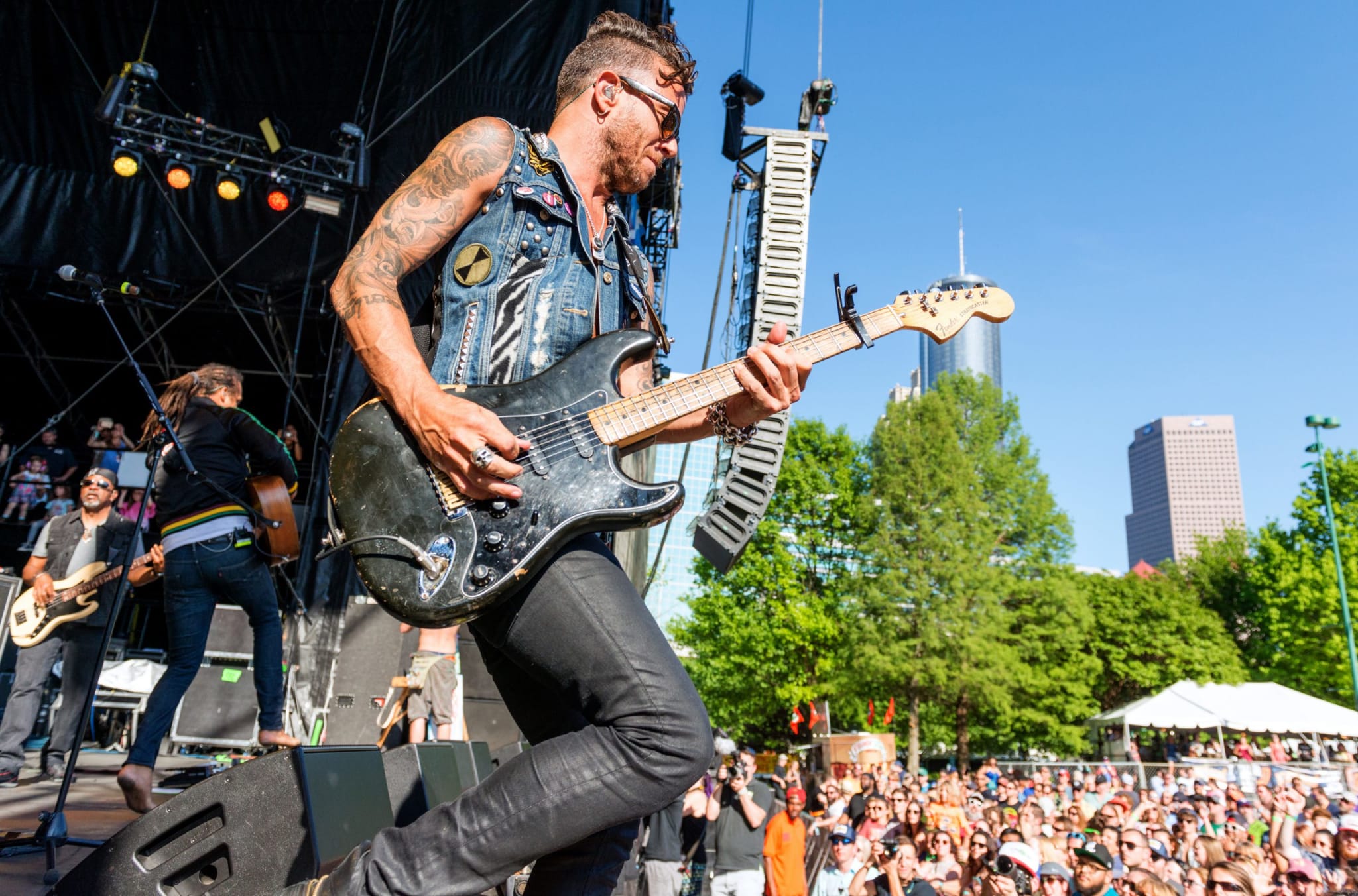 A musician with tattoos plays an electric guitar on stage at an outdoor concert in Atlanta, Georgia.