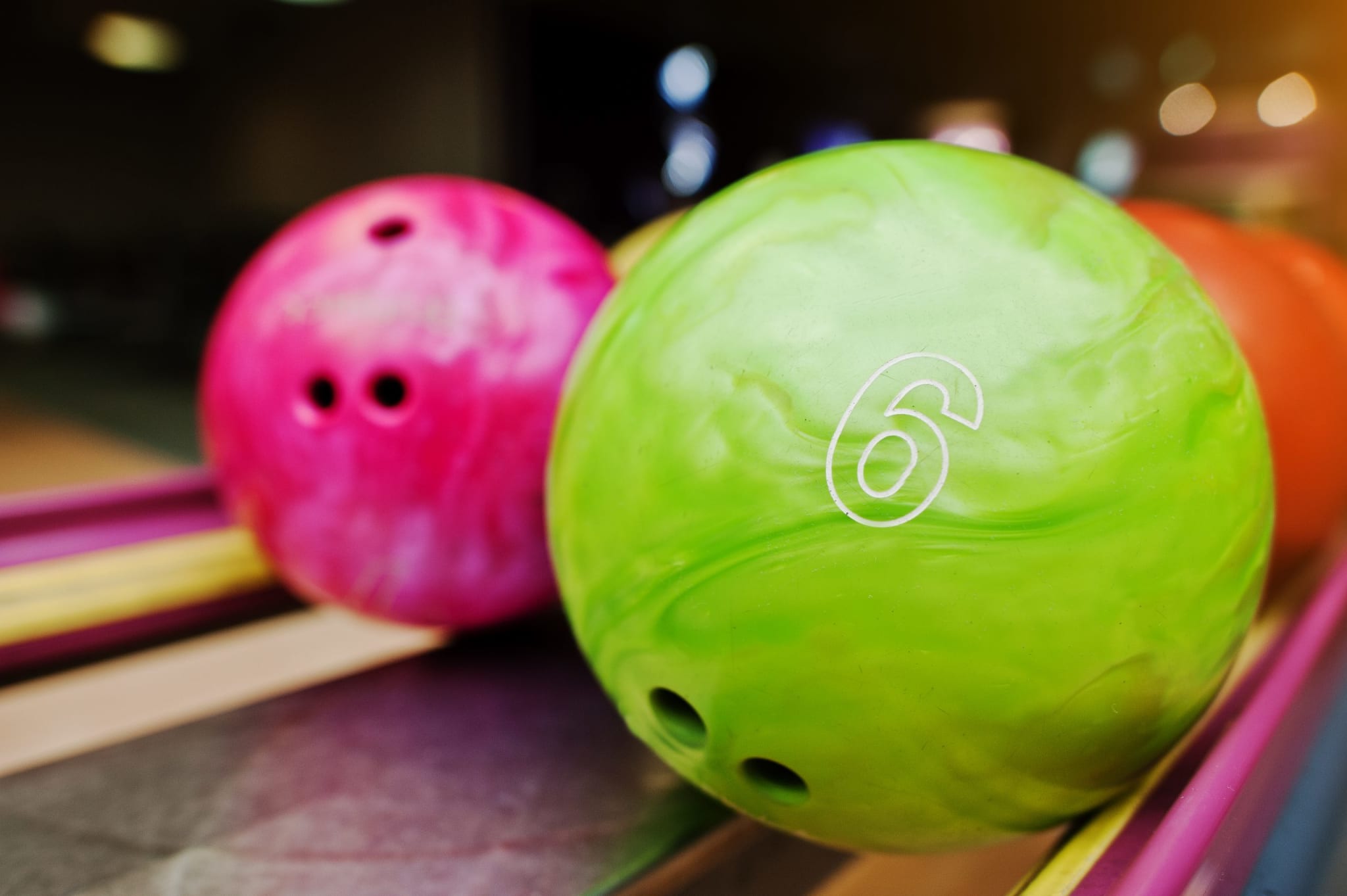 Two bowling balls, one pink and one green with a number 6, sit on a rack at a bowling alley in Atlanta, Georgia.