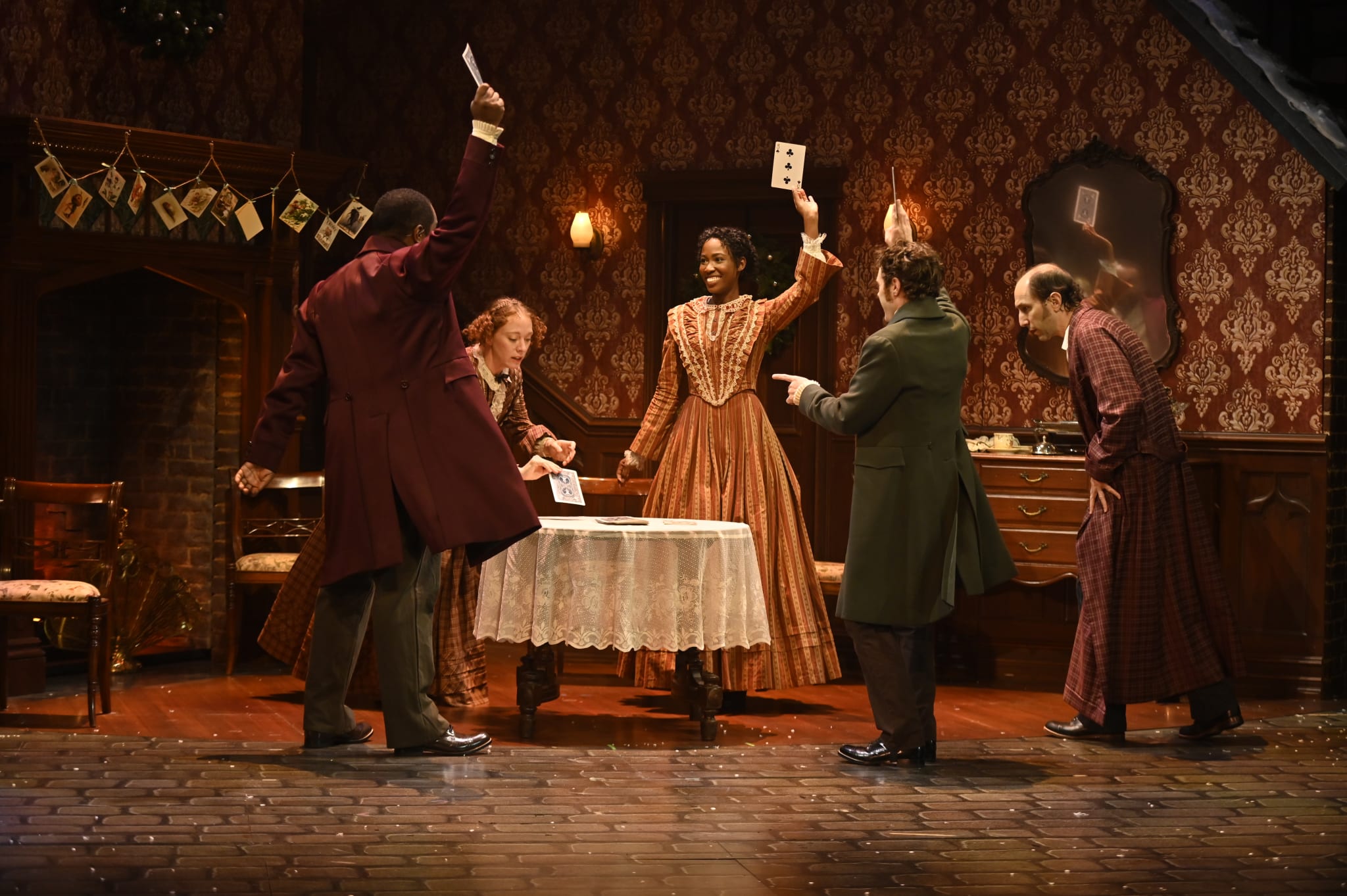 A group of five people in Victorian-era costumes play cards in a dimly lit room with ornate wallpaper in Atlanta, Georgia.