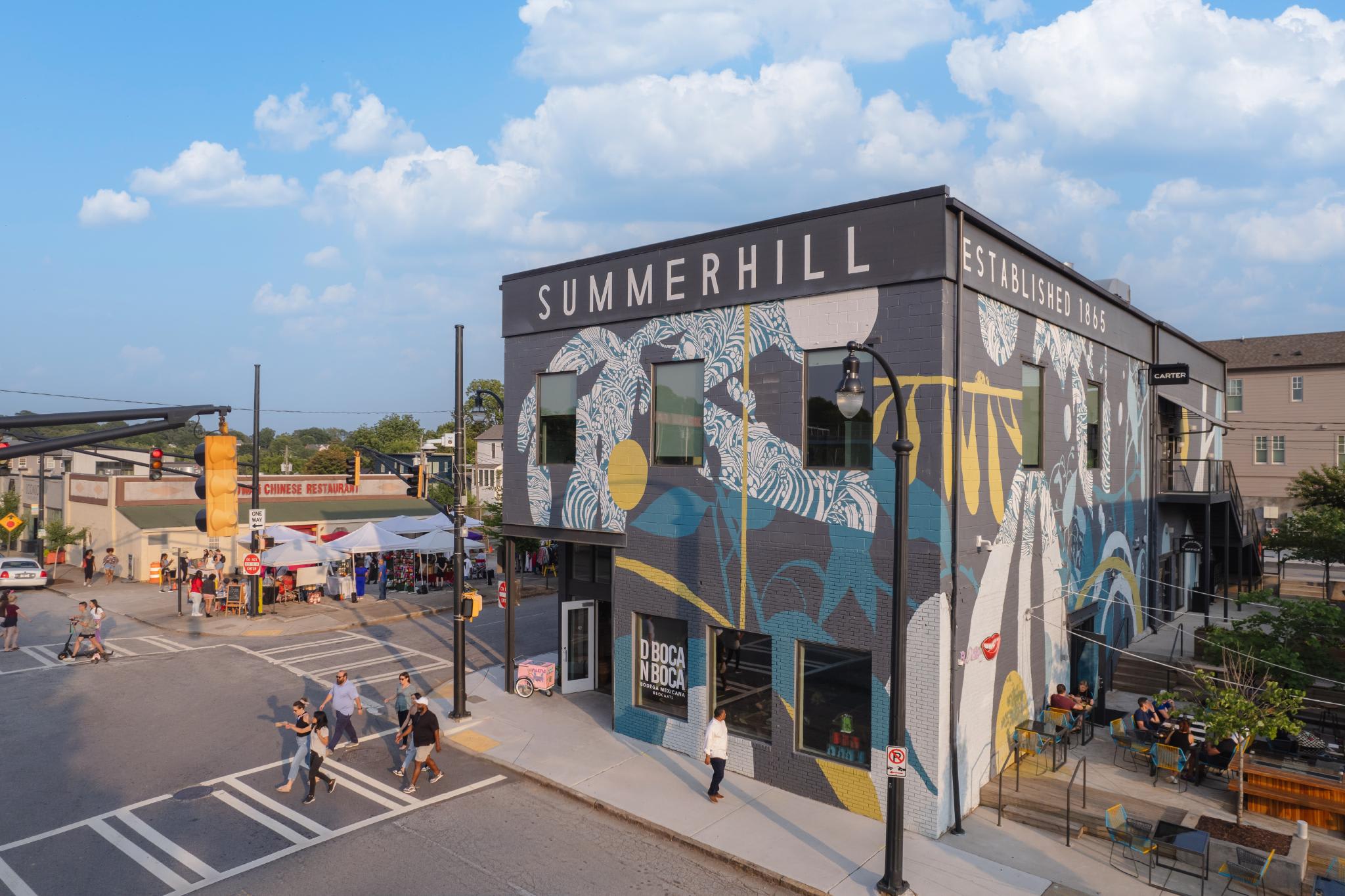 @DiscoverAtlanta Link In Bio 51 A vibrant mural adorns the side of a building in a bustling town square, with pedestrians and street vendors below in Atlanta, Georgia.