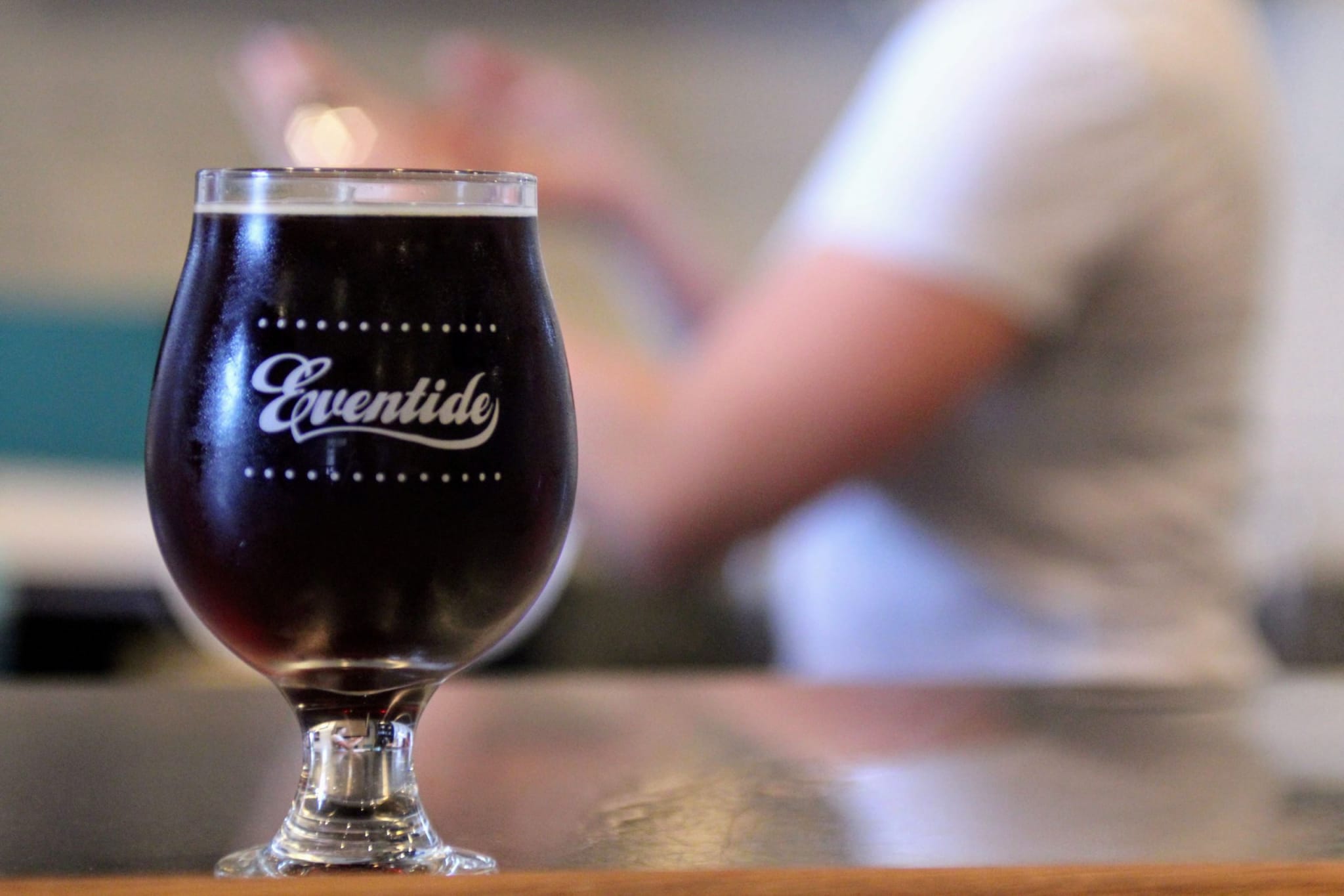 A dark beer in a tulip glass with 'Eventide' branding sits on a wooden bar in Atlanta, Georgia.
