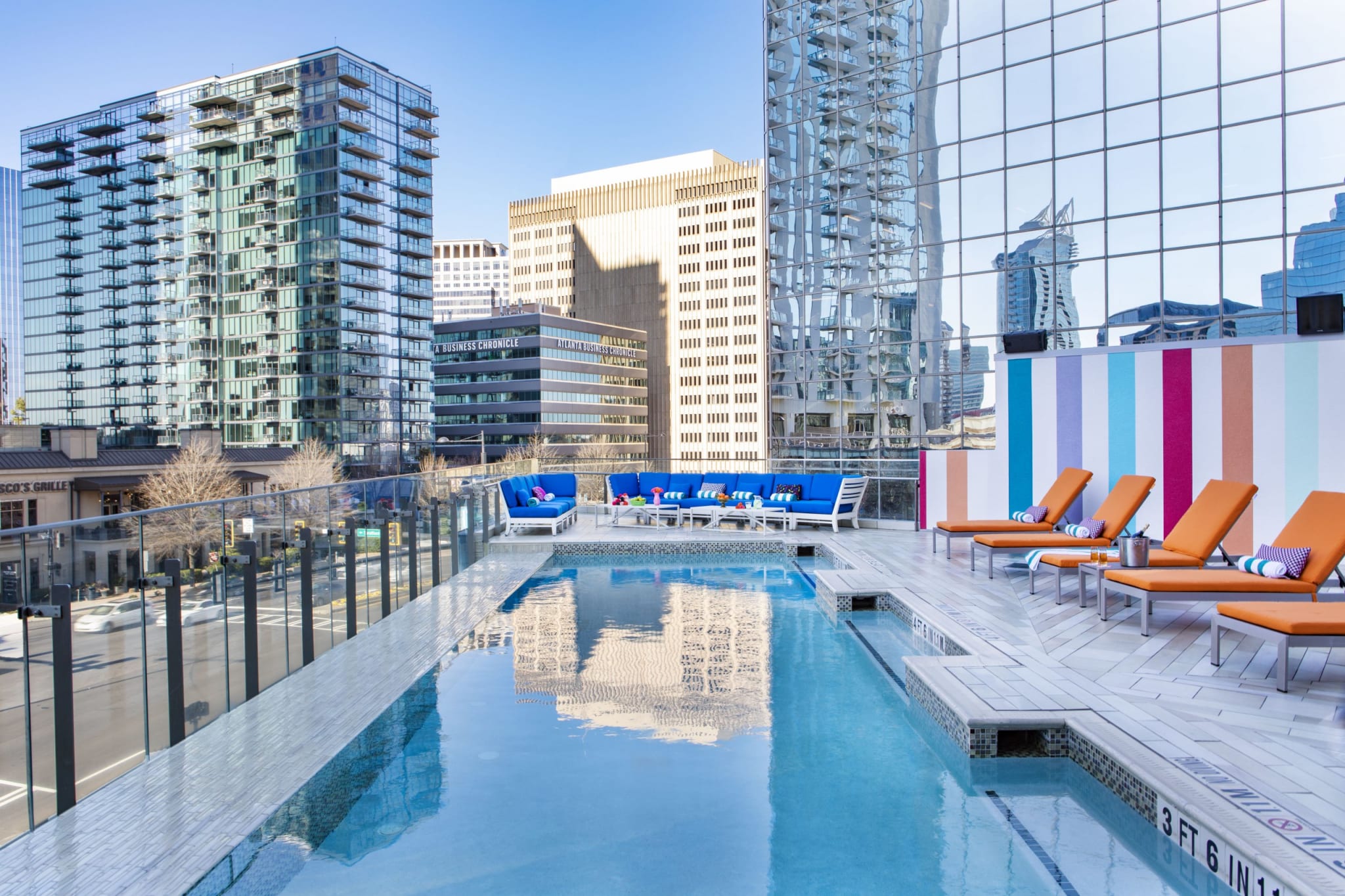 A rooftop pool area with orange lounge chairs and blue seating overlooks a city skyline in Atlanta, Georgia.