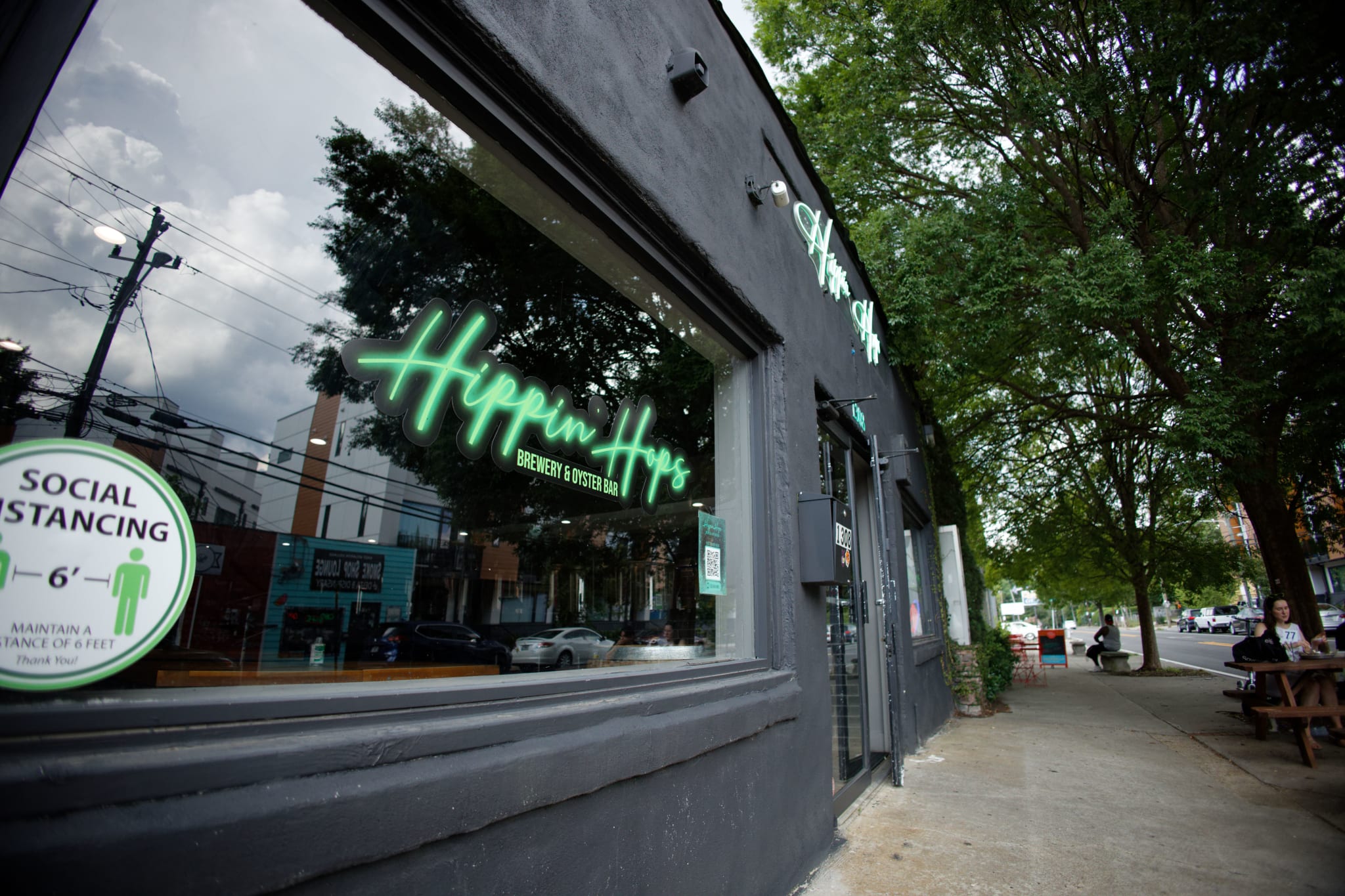 A black building with a neon sign reading 'Hippin' Hops' and a social distancing sticker on the window in Atlanta, Georgia.