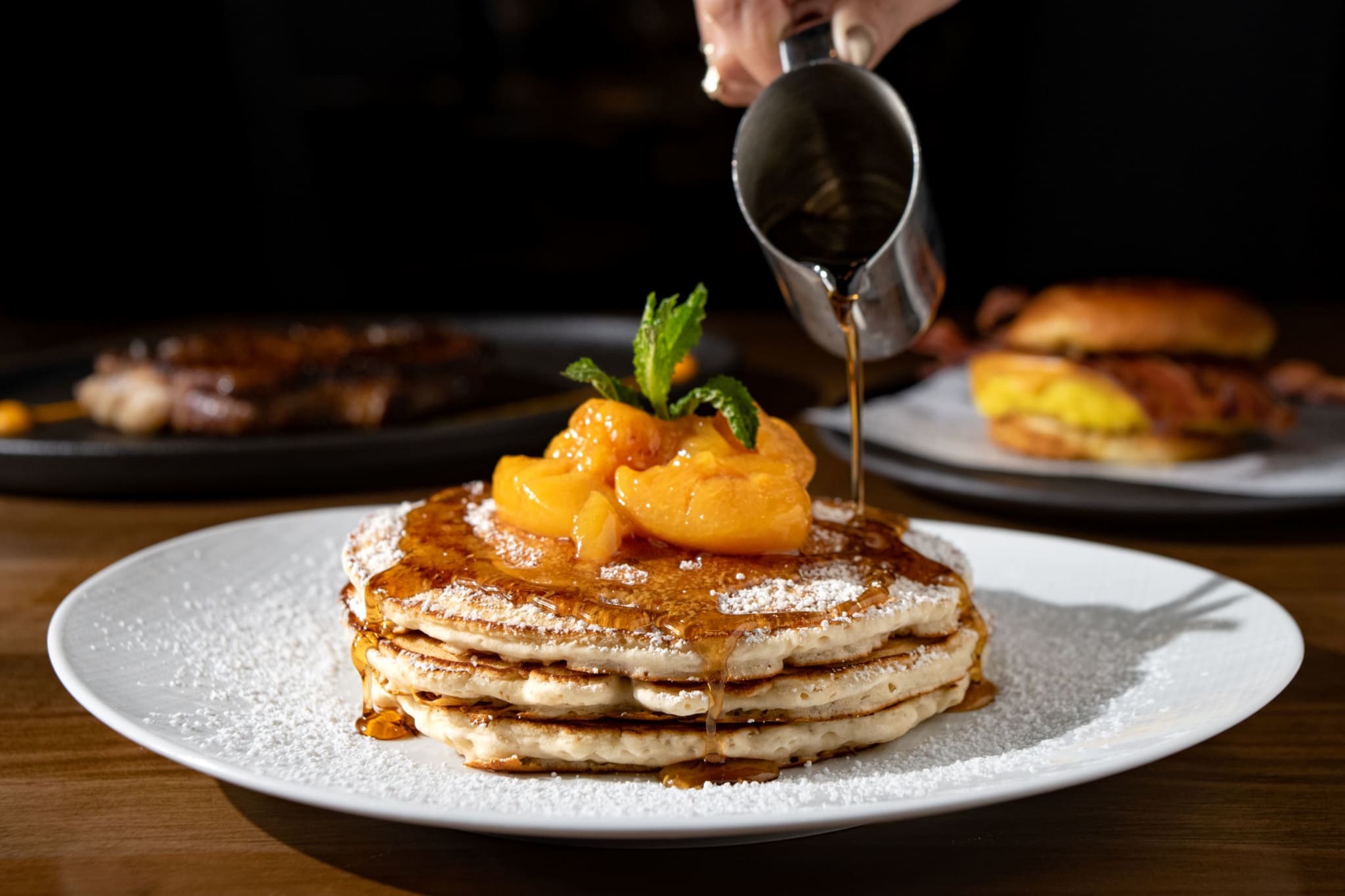 A stack of fluffy pancakes topped with caramelized peaches and drizzled with syrup in Atlanta, Georgia.