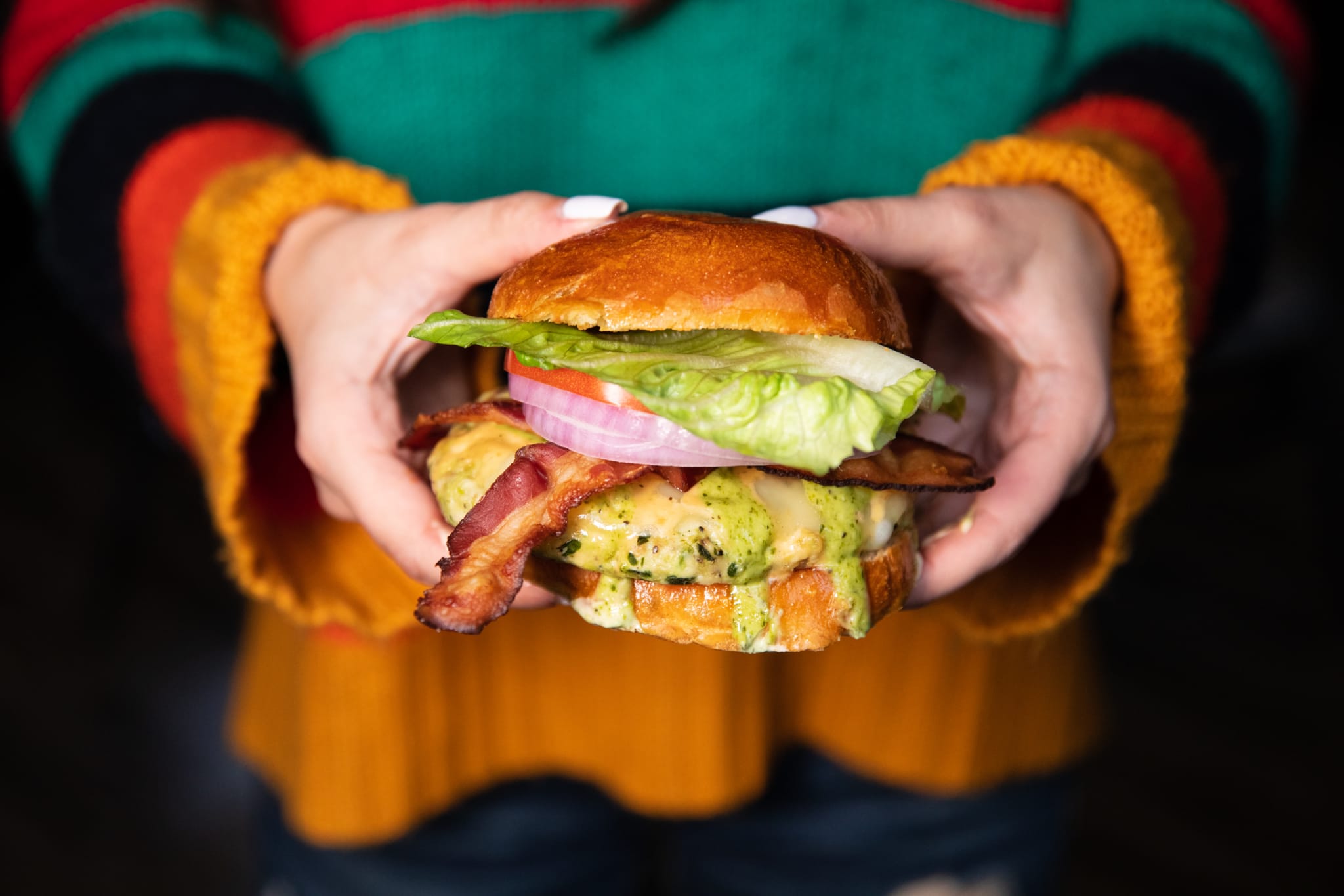 A person holds a mouthwatering bacon cheeseburger with lettuce, tomato, and onion in Atlanta, Georgia.