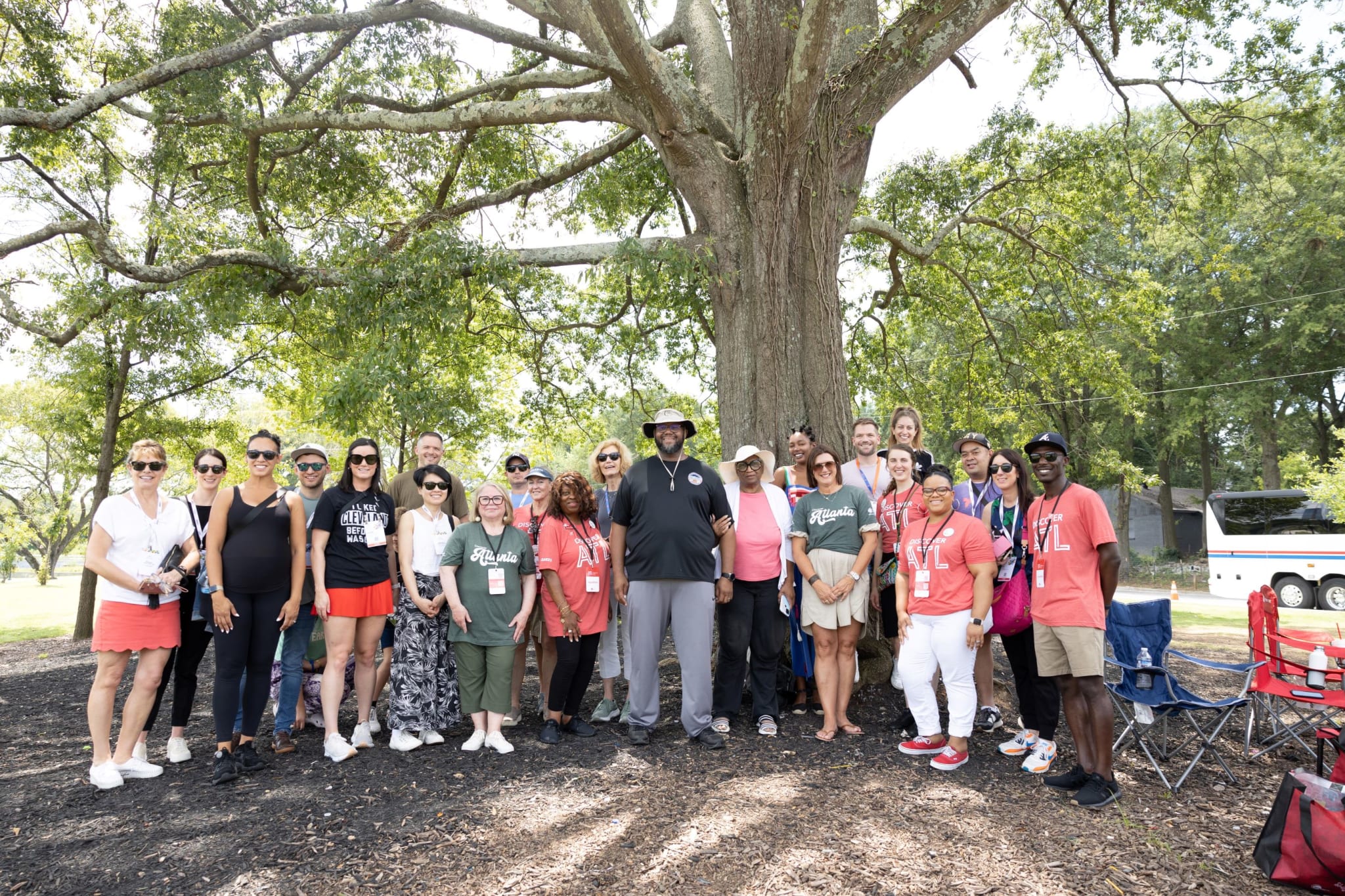 A diverse group of people wearing matching shirts gather under a large tree in a park in Atlanta, Georgia.