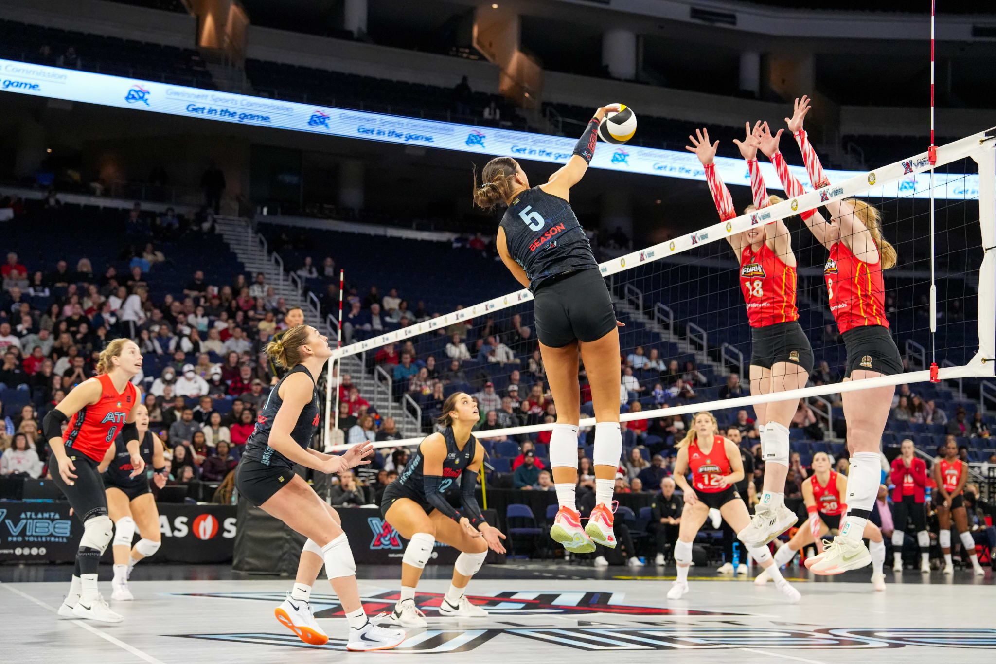 Volleyball players in action during a competitive match, with one player spiking the ball over the net in Atlanta, Georgia.