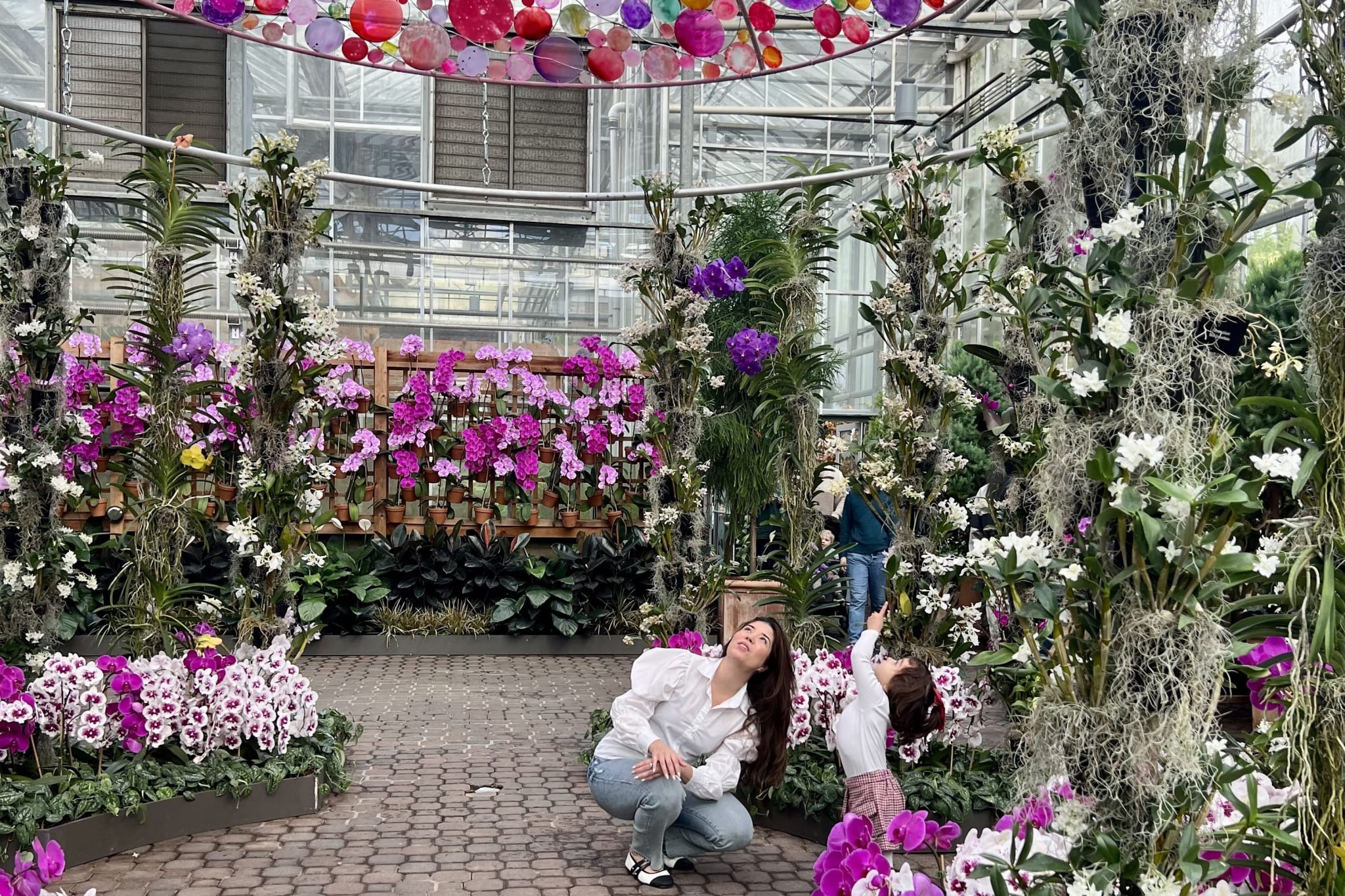 A woman and child kneel amidst a vibrant indoor garden filled with colorful flowers and lush greenery in Atlanta, Georgia.