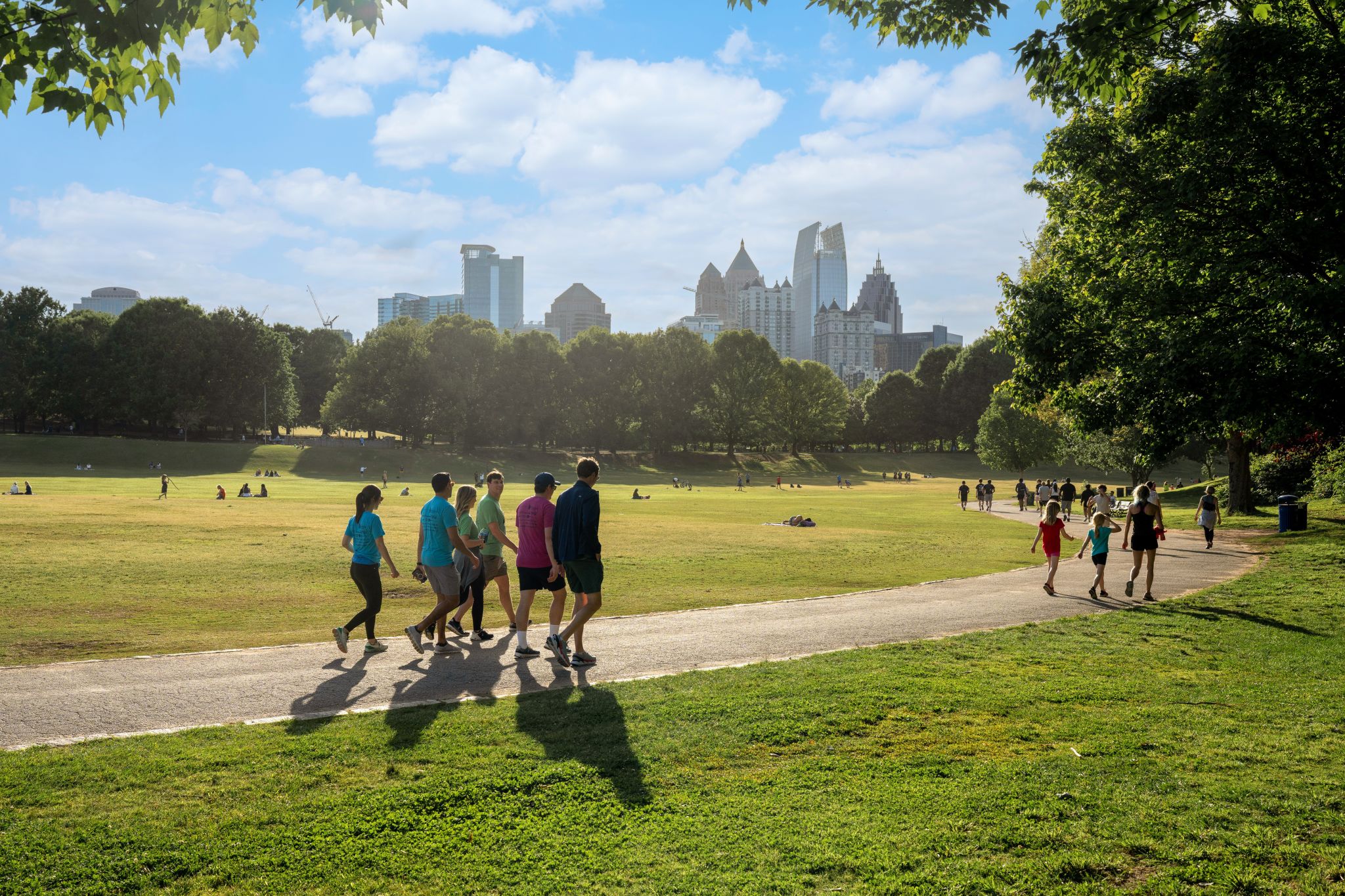 A group of people walks along a path in a park with a city skyline in the background in Atlanta, Georgia.
