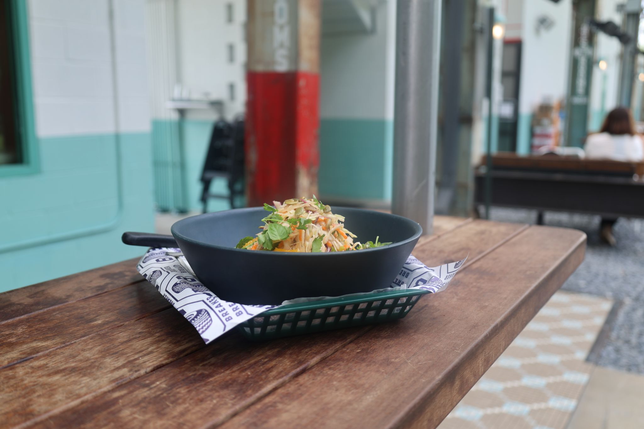 A black bowl of salad with colorful vegetables sits on a wooden table outdoors in Atlanta, Georgia.