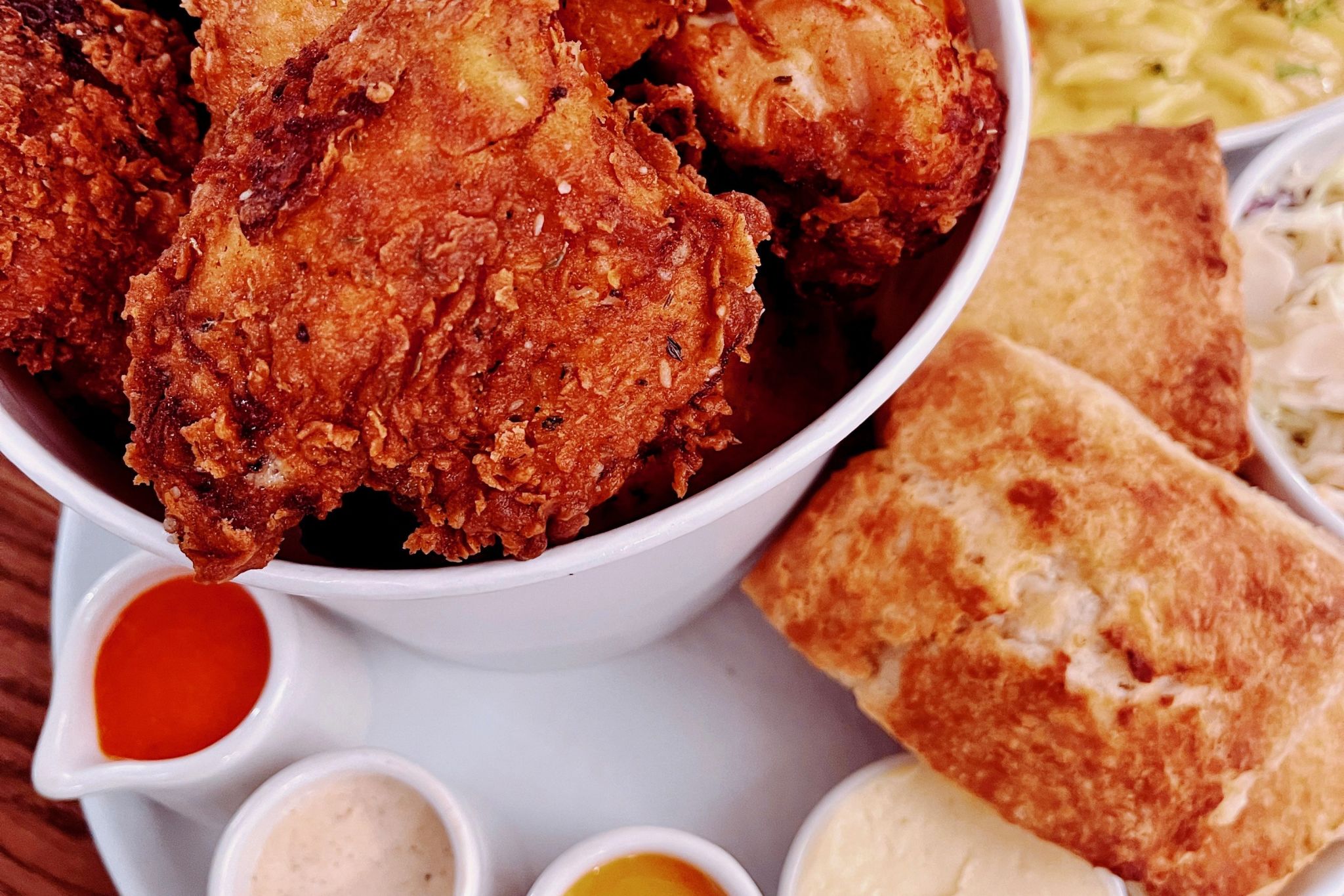 A hearty meal featuring a large bowl of crispy fried chicken, accompanied by macaroni and cheese, biscuits, coleslaw, and a variety of dipping sauces including hot, honey mustard, ranch, and barbecue in Atlanta, Georgia.