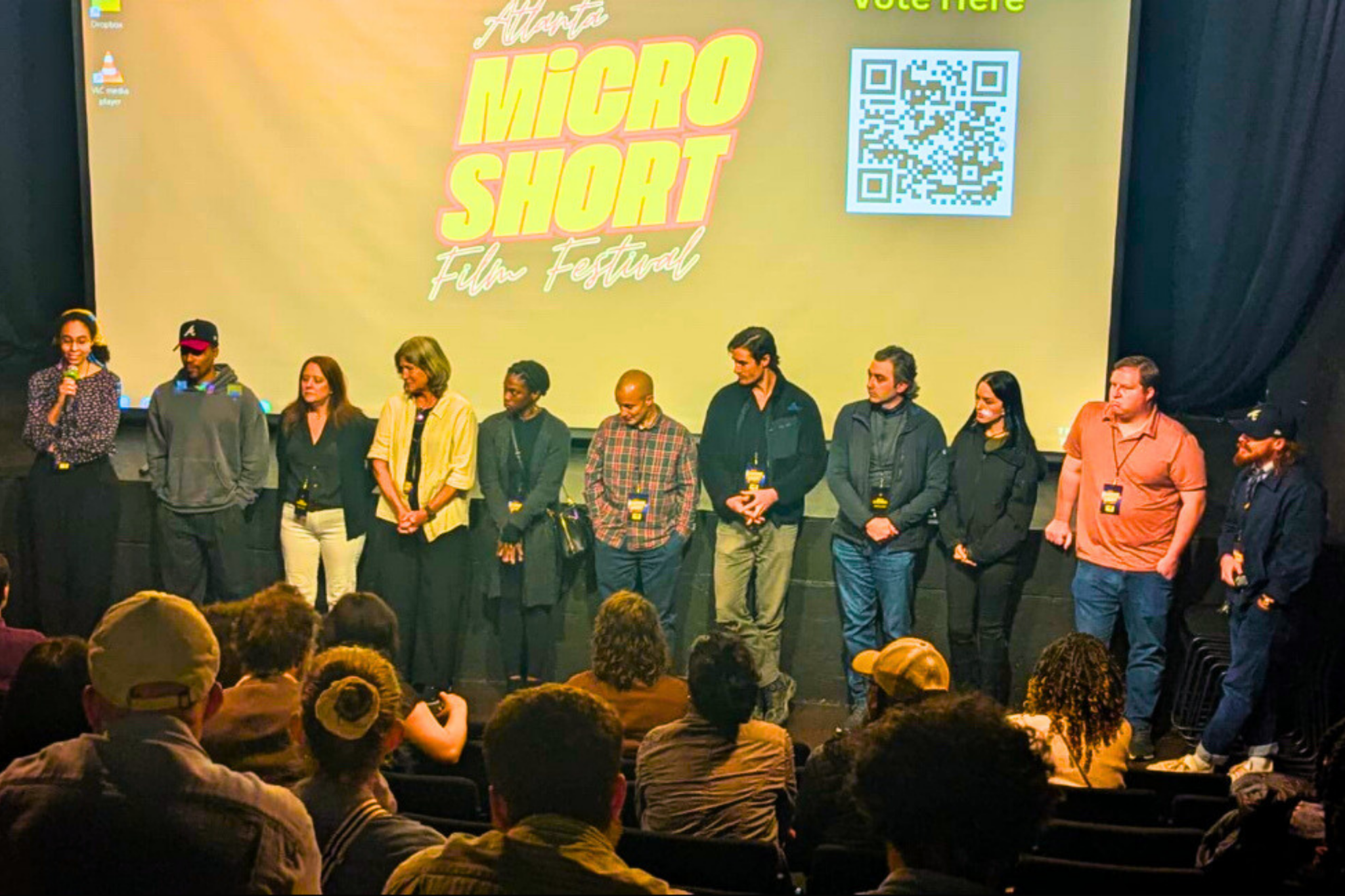 A diverse group of filmmakers and festival organizers stand on stage at the Atlanta Micro Short Film Festival, addressing an engaged audience in Atlanta, Georgia.