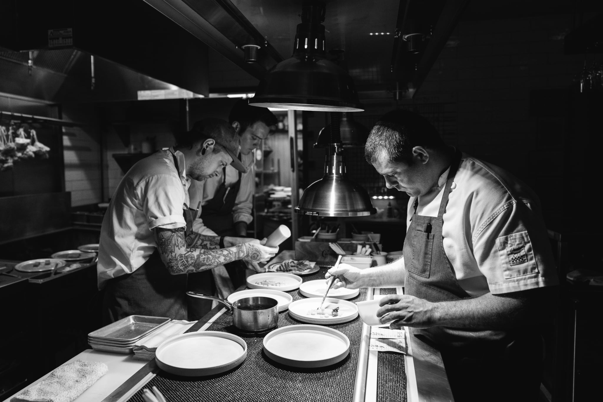 Three chefs in a dimly lit kitchen preparing food on white plates in Atlanta, Georgia.